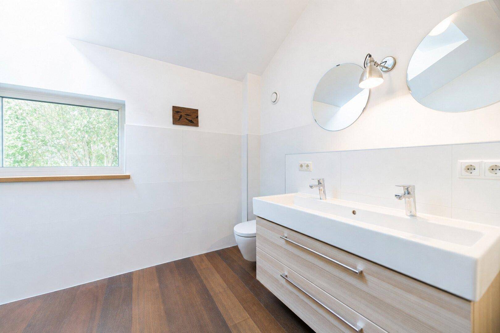 Helles Badezimmer mit Doppelwaschbecken, Wand-WC und Holzfußboden.