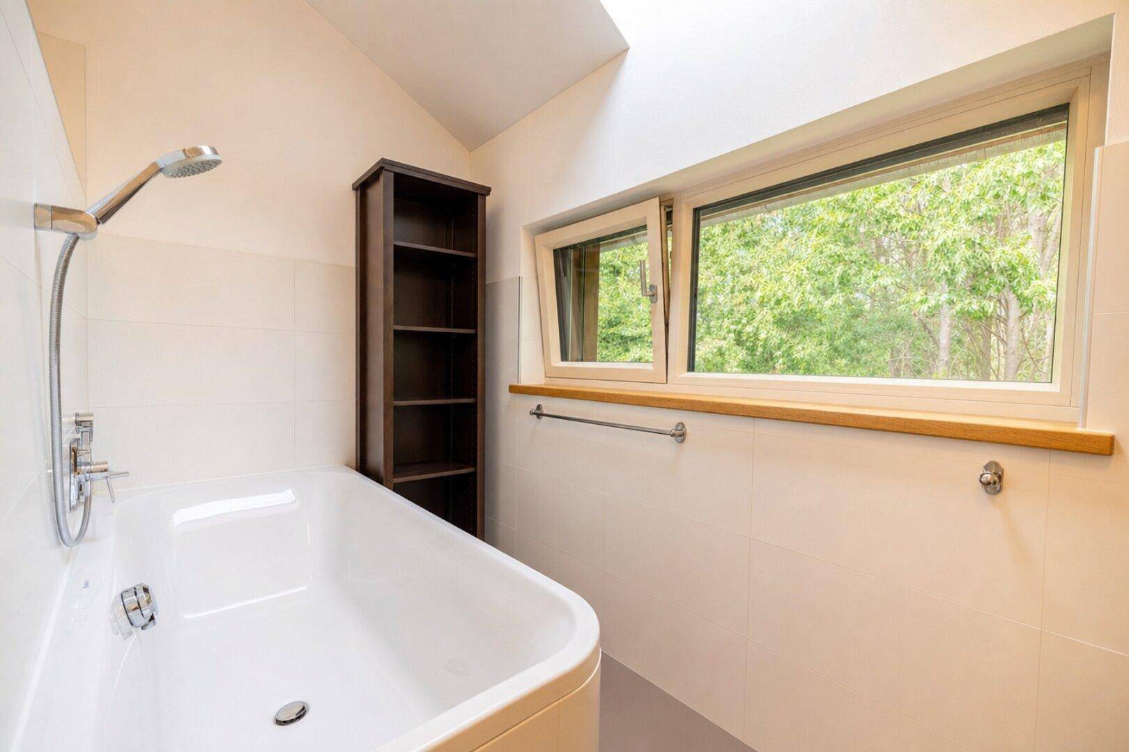 Modernes Badezimmer mit Badewanne, Dusche und Fenster mit Blick ins Grüne.