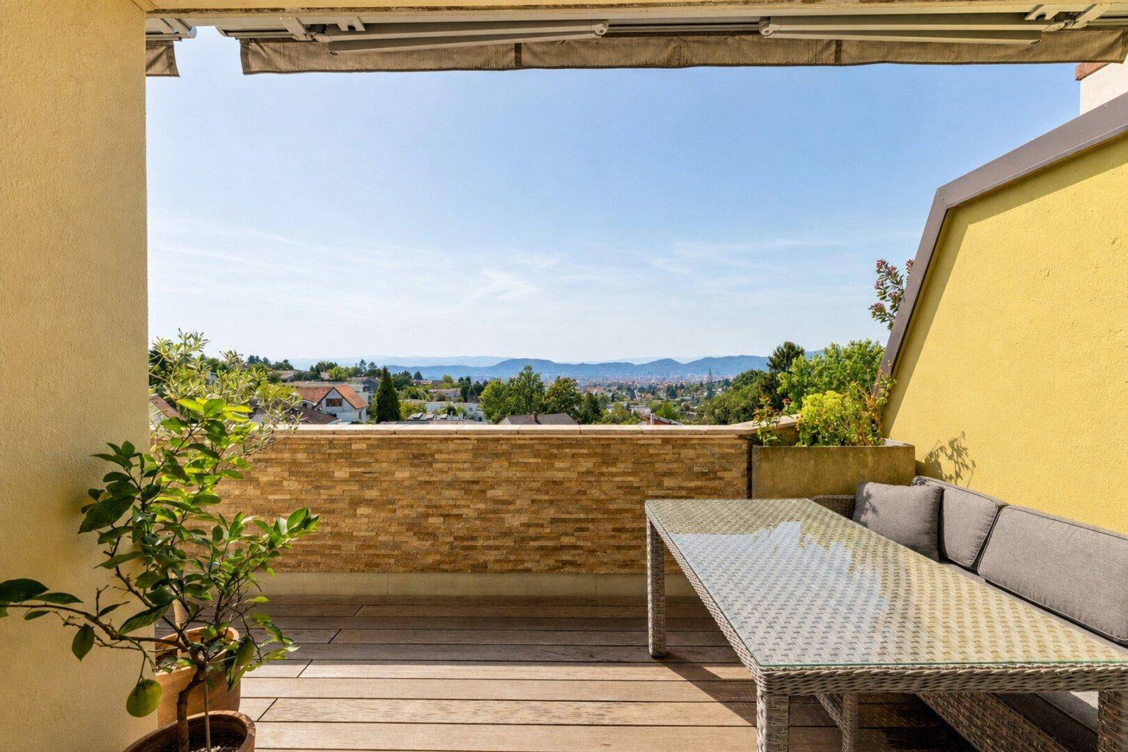 Sonnige Terrasse mit Holzboden, bequemen Gartenmöbeln und weitem Blick über die Stadt und Berge.