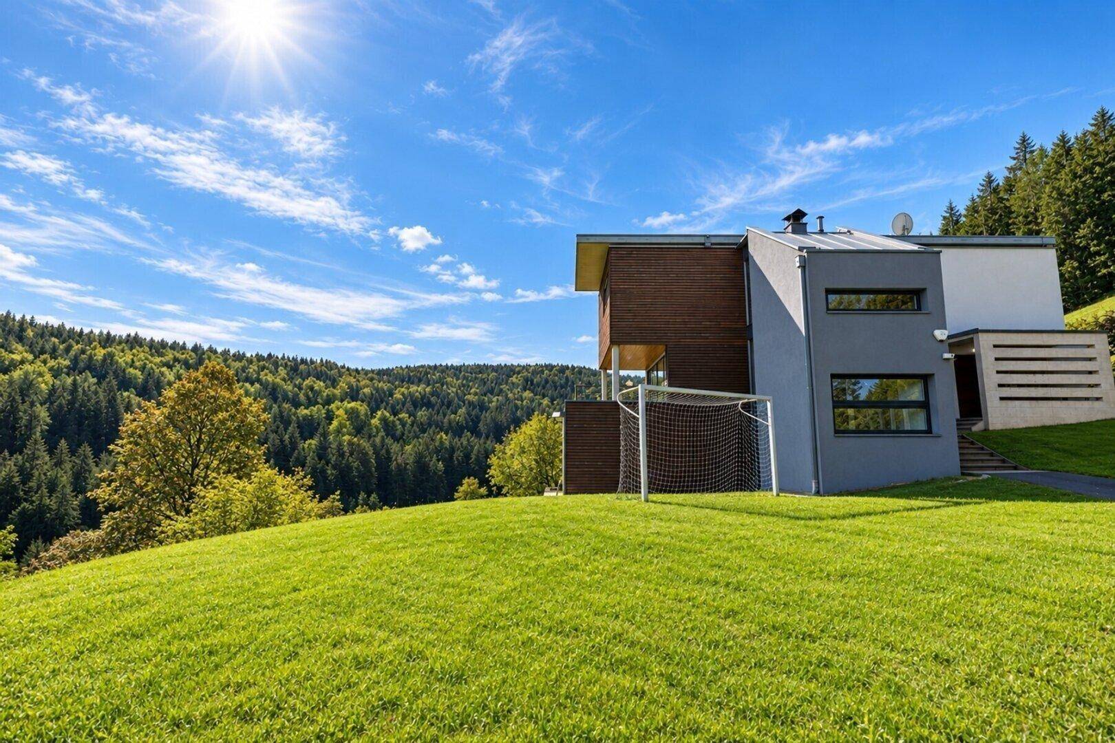 Modernes Haus mit weitläufigem Rasen und Blick auf die umliegende Waldlandschaft an einem sonnigen Tag.