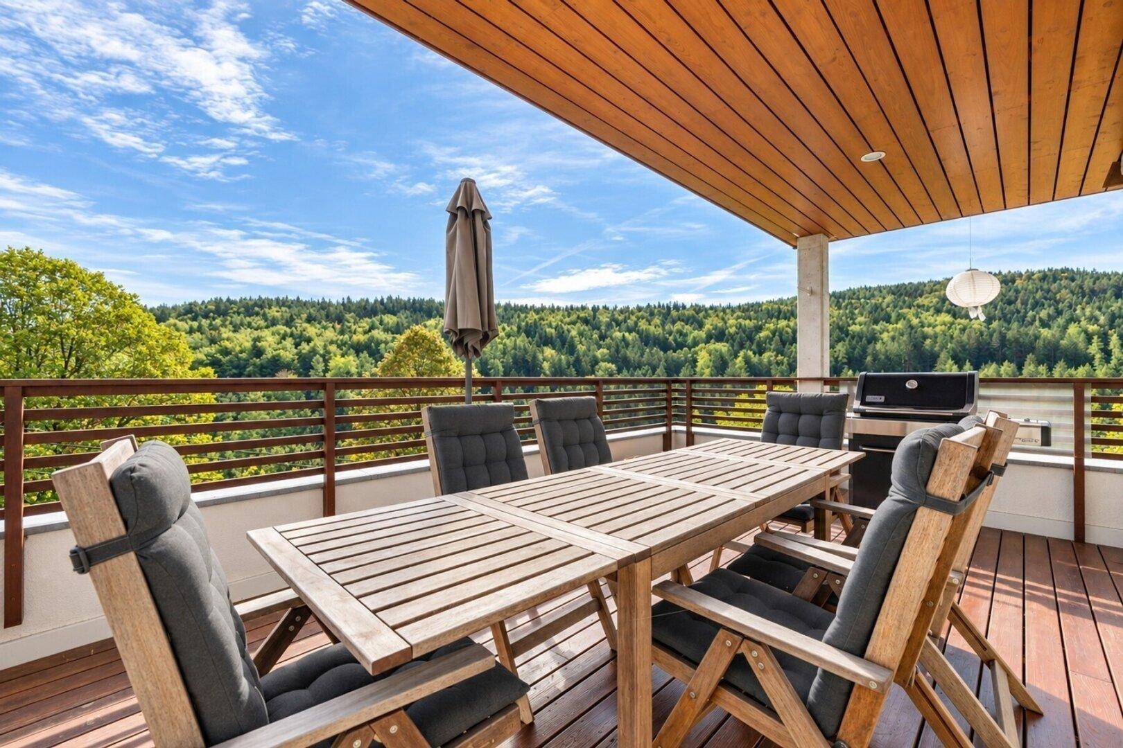 Überdachte Terrasse mit Holztisch, Stühlen und Grill, perfekt für gesellige Abende im Freien.