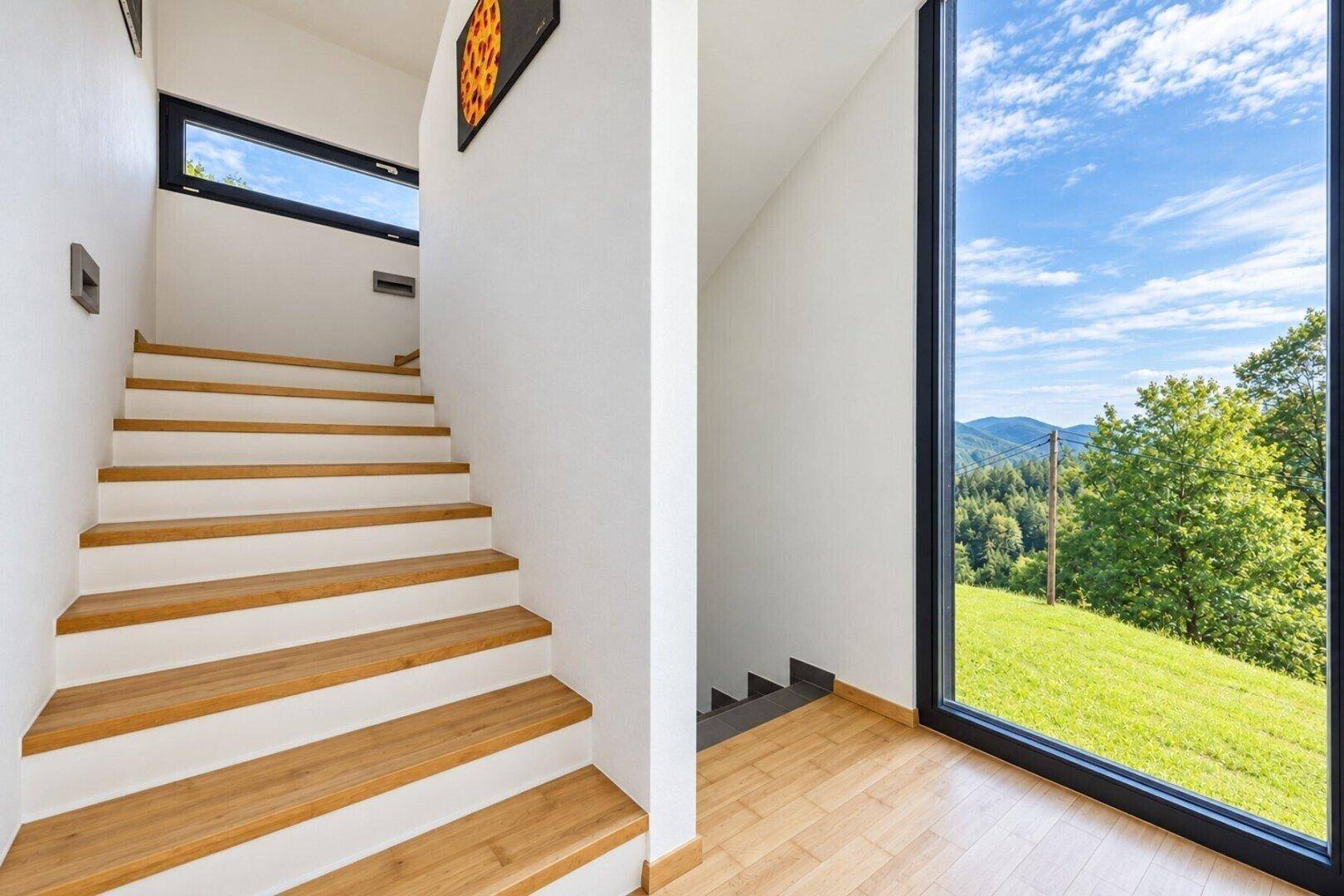 Heller Treppenaufgang mit Holzstufen und großem Fenster, das viel Tageslicht hereinlässt.