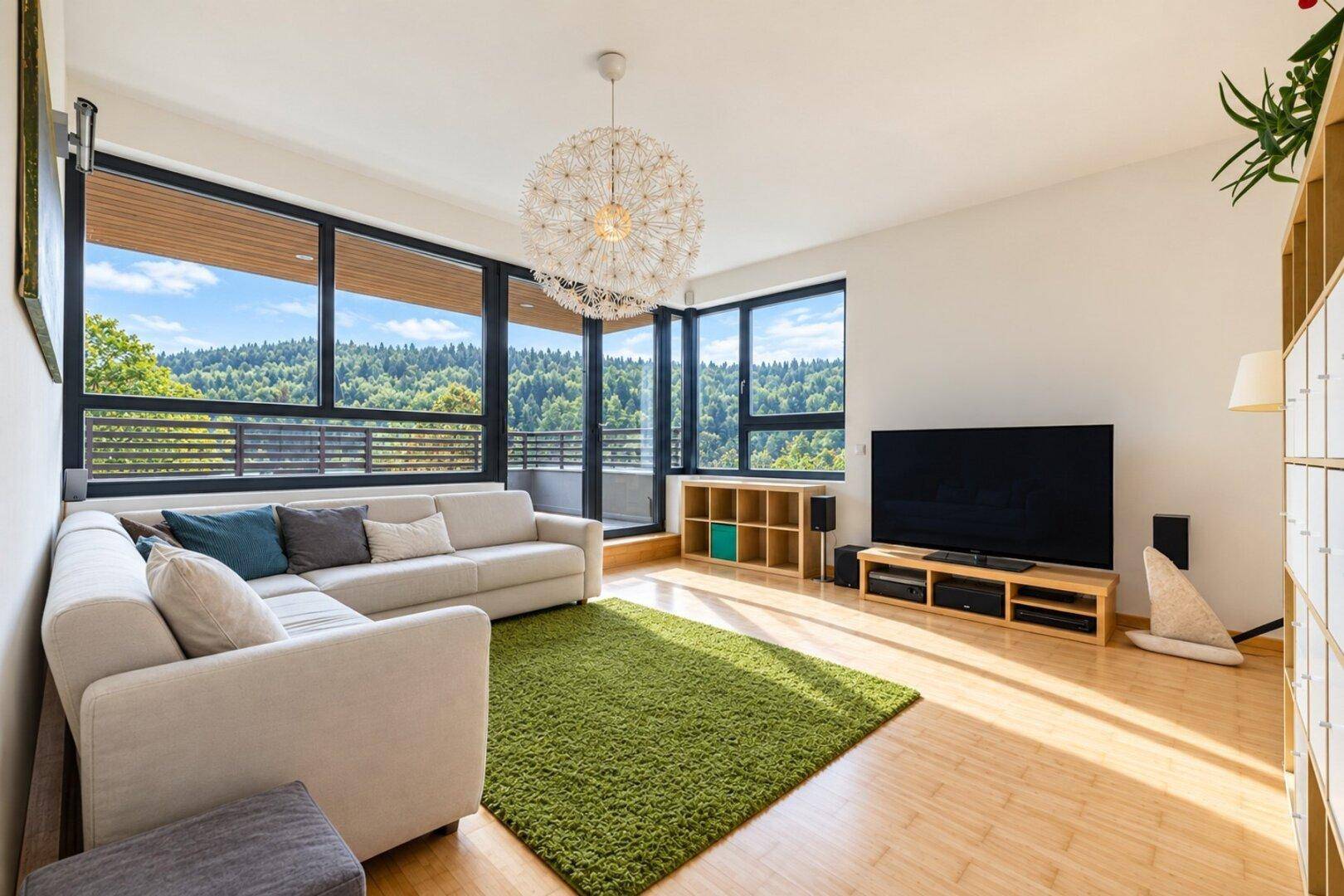 Helles Wohnzimmer mit großen Fenstern, die einen weiten Blick auf die bewaldete Landschaft bieten.