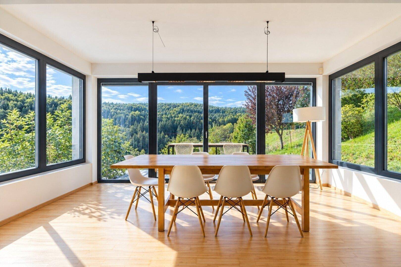 Geräumiger Essbereich mit Holztisch und Stühlen, umgeben von bodentiefen Fenstern mit Waldblick.