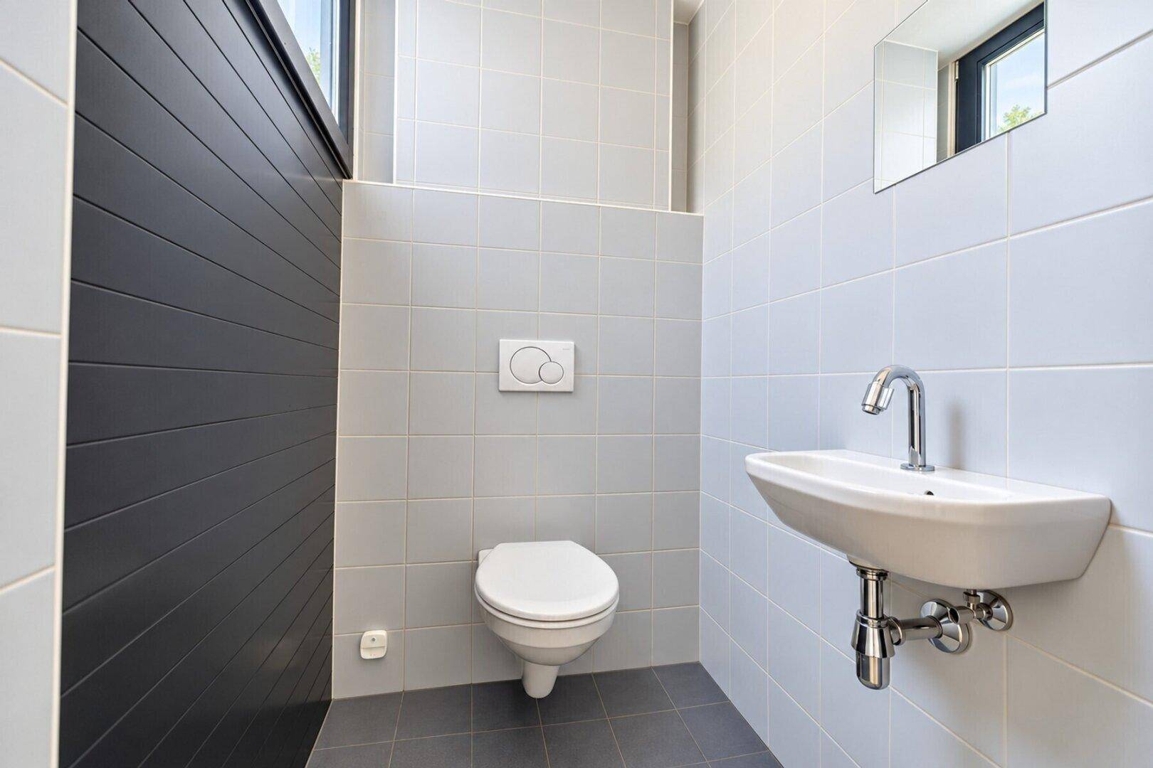 Modernes Gäste-WC mit wandhängender Toilette und kleinem Waschbecken, in schlichtem Design.