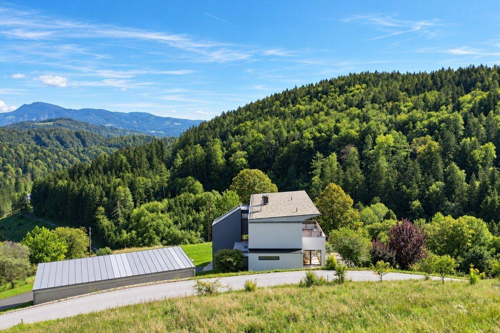 Weitläufige Luftaufnahme des Anwesens mit Haus, Garage und umliegender grüner Hügellandschaft.