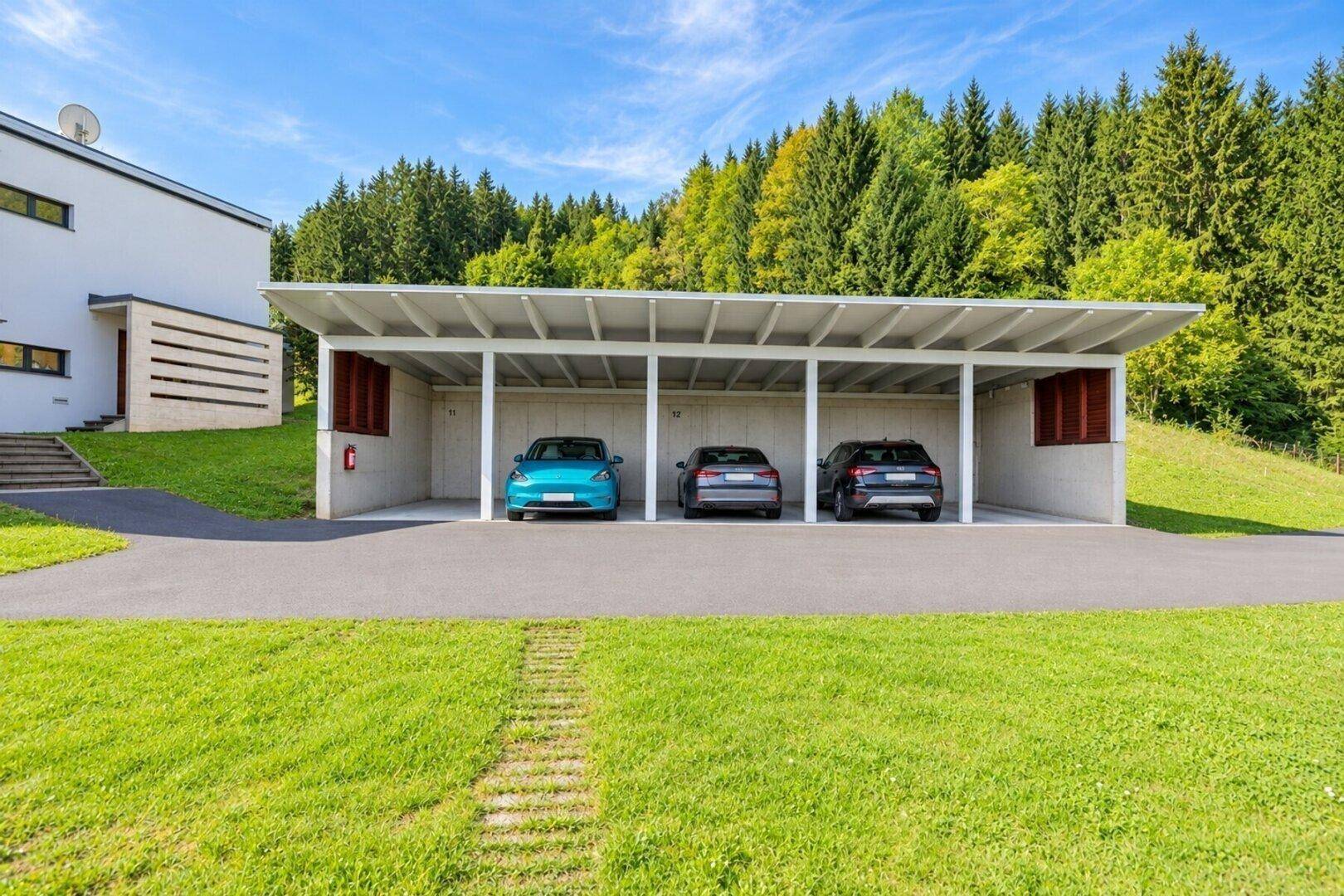 Überdachter Carport mit Stellplätzen für mehrere Fahrzeuge, umgeben von Rasenflächen.