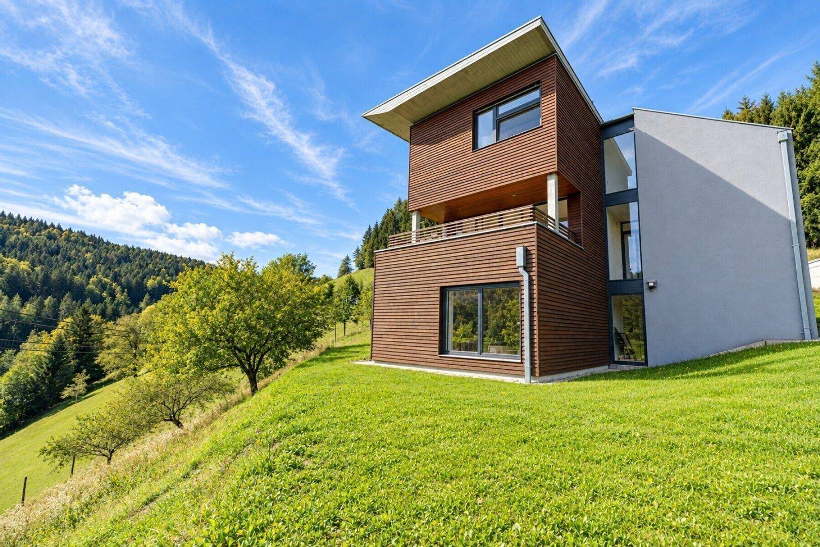 Moderne Architektur des Hauses mit Holz- und Putzfassade, großen Fenstern und Balkonen.