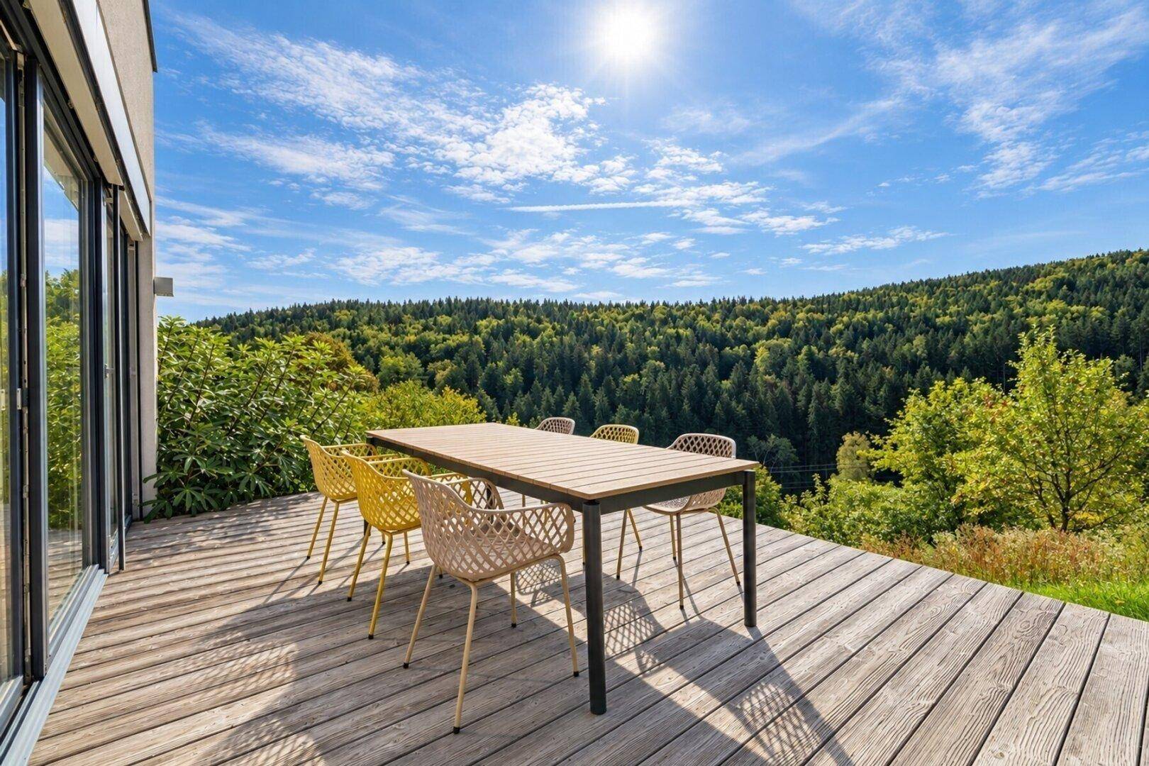 Sonniger Terrassenbereich mit Holzboden und Esstisch, ideal für Mahlzeiten im Freien mit Waldblick.