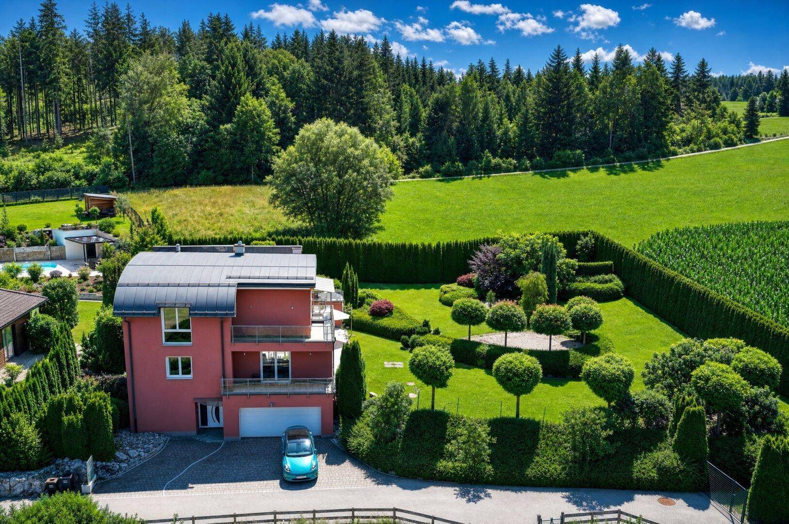 Luftaufnahme der modernen Villa mit weitläufigem Garten, umgeben von grünen Feldern und Wald.