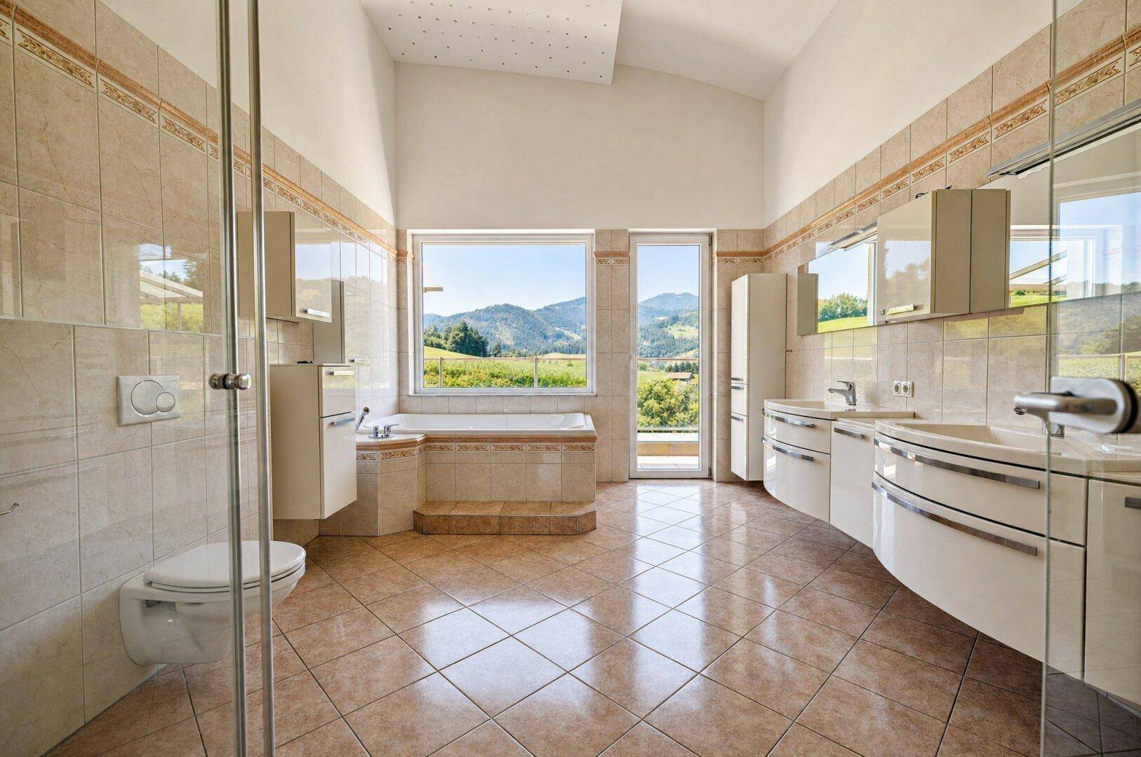 Großzügiges Badezimmer mit Badewanne, Doppelwaschbecken und Panoramablick auf die Landschaft.