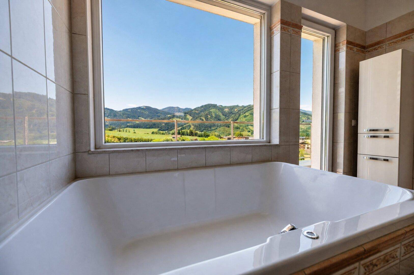 Badewanne mit entspannendem Ausblick auf die grüne Hügellandschaft durch das große Fenster.