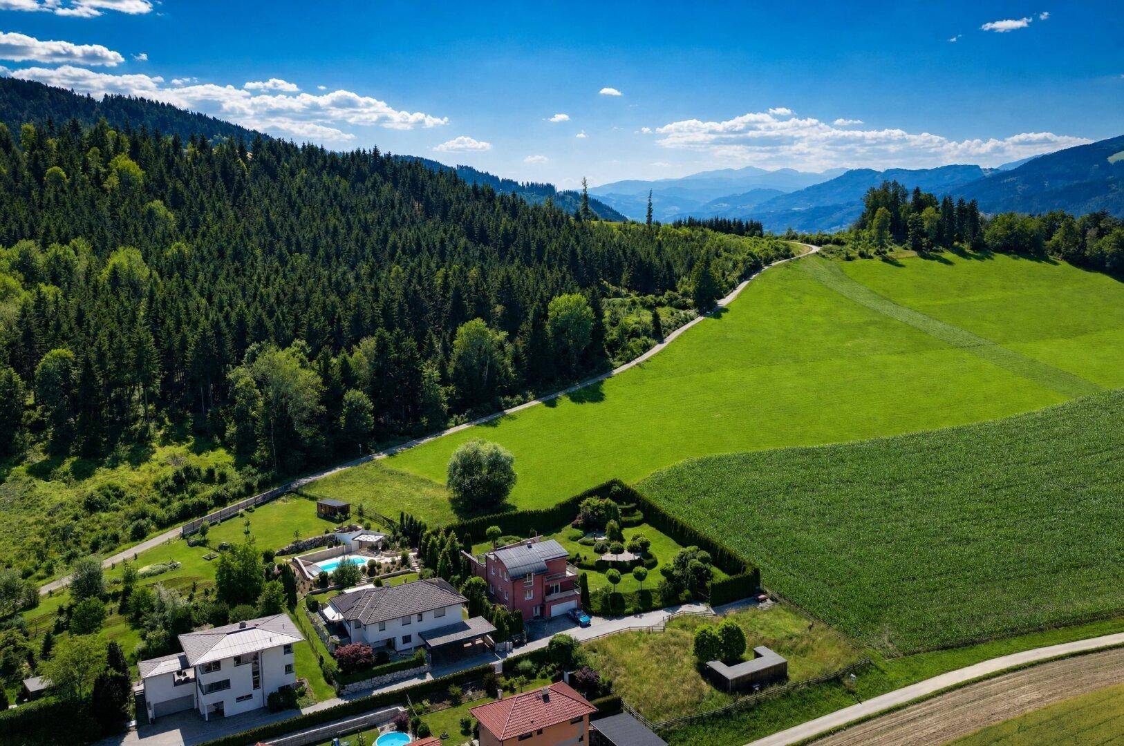 Luftaufnahme einer Wohnsiedlung mit gepflegten Gärten, Pools und angrenzenden Wäldern und Feldern.