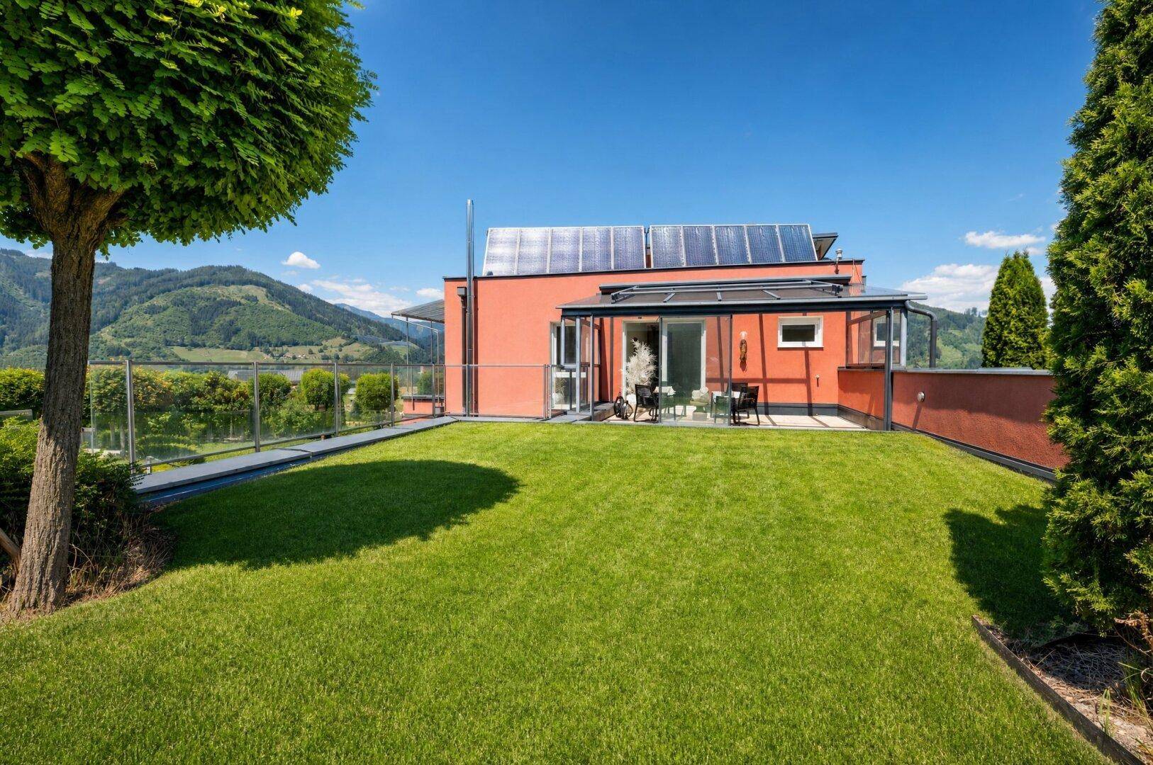 Rückseite eines modernen Hauses mit gepflegtem Rasen, Terrasse und Solarpaneelen auf dem Dach.