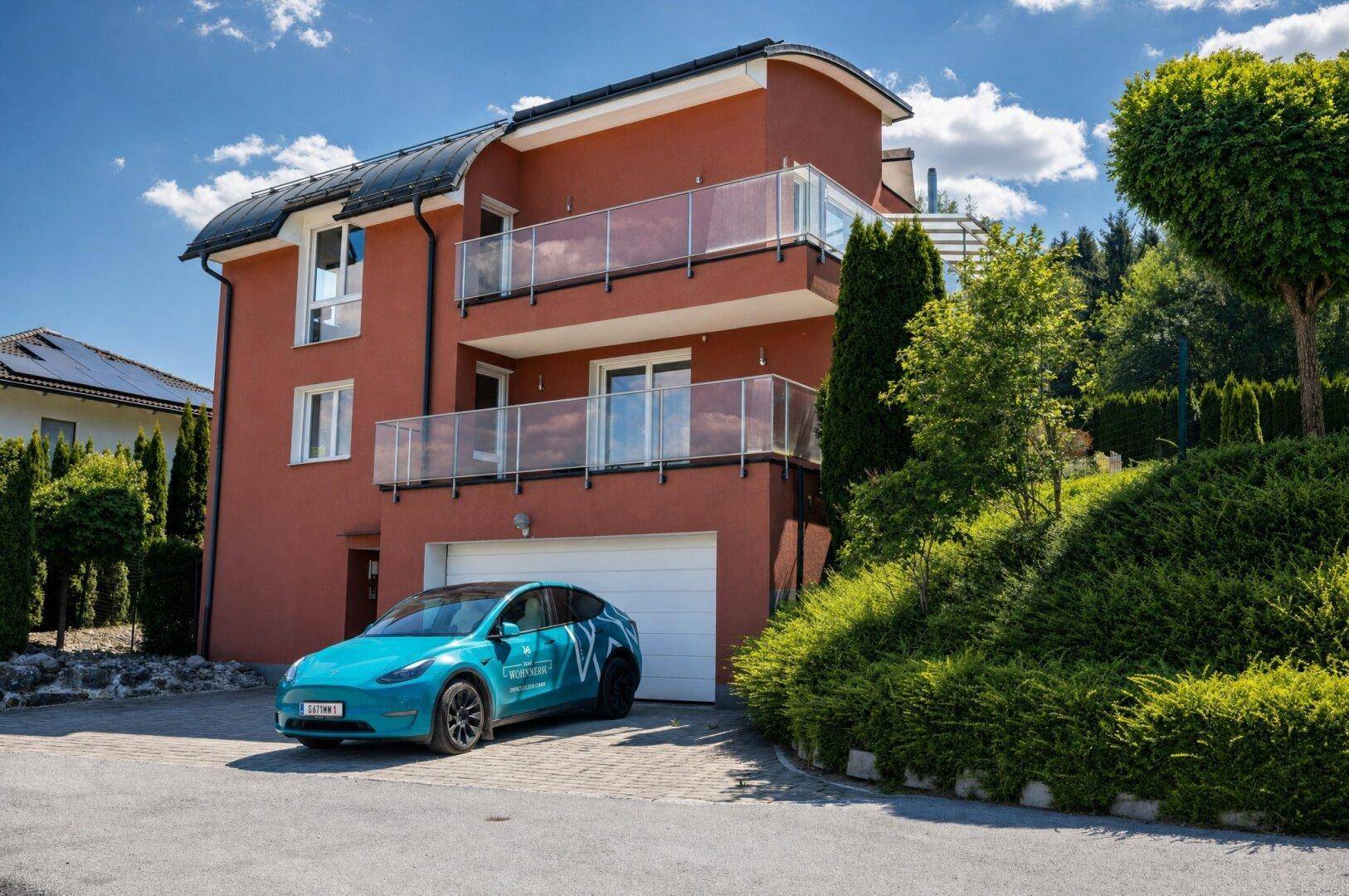 Attraktives Wohnhaus mit roter Fassade, mehreren Balkonen mit Glasgeländer und einer Garage.
