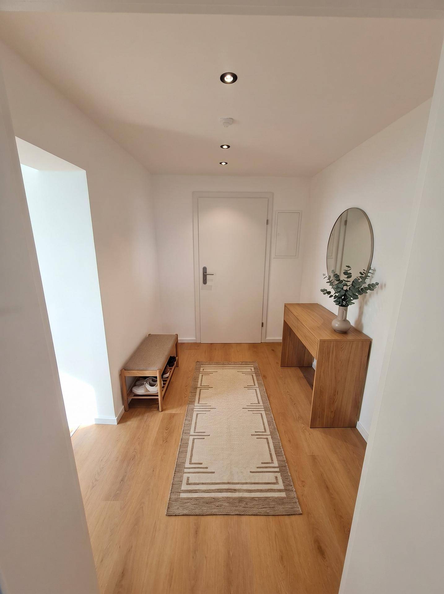 Freundlicher Eingangsbereich mit Holzboden, Spiegel und Ablagemöglichkeit, modern eingerichtet.