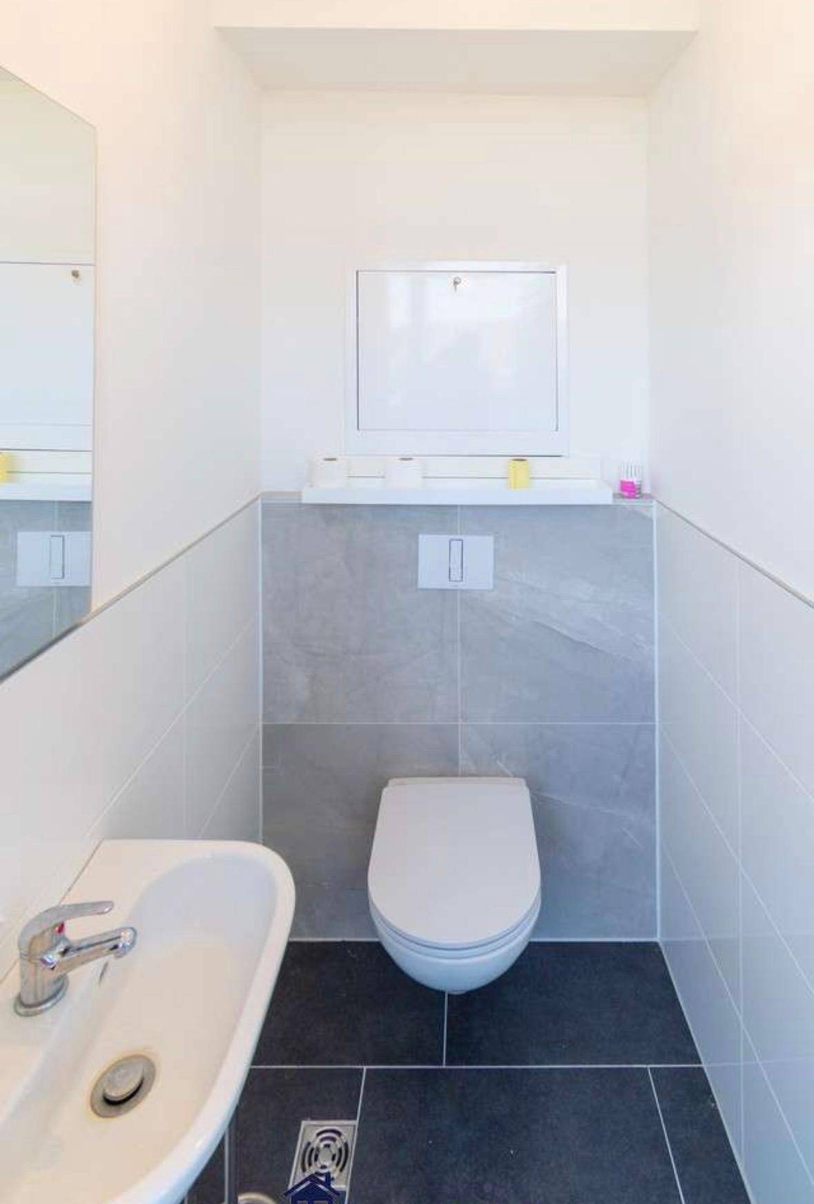 Helles Gäste-WC mit weiß-grauen Fliesen, wandhängendem WC und kleinem Waschbecken.