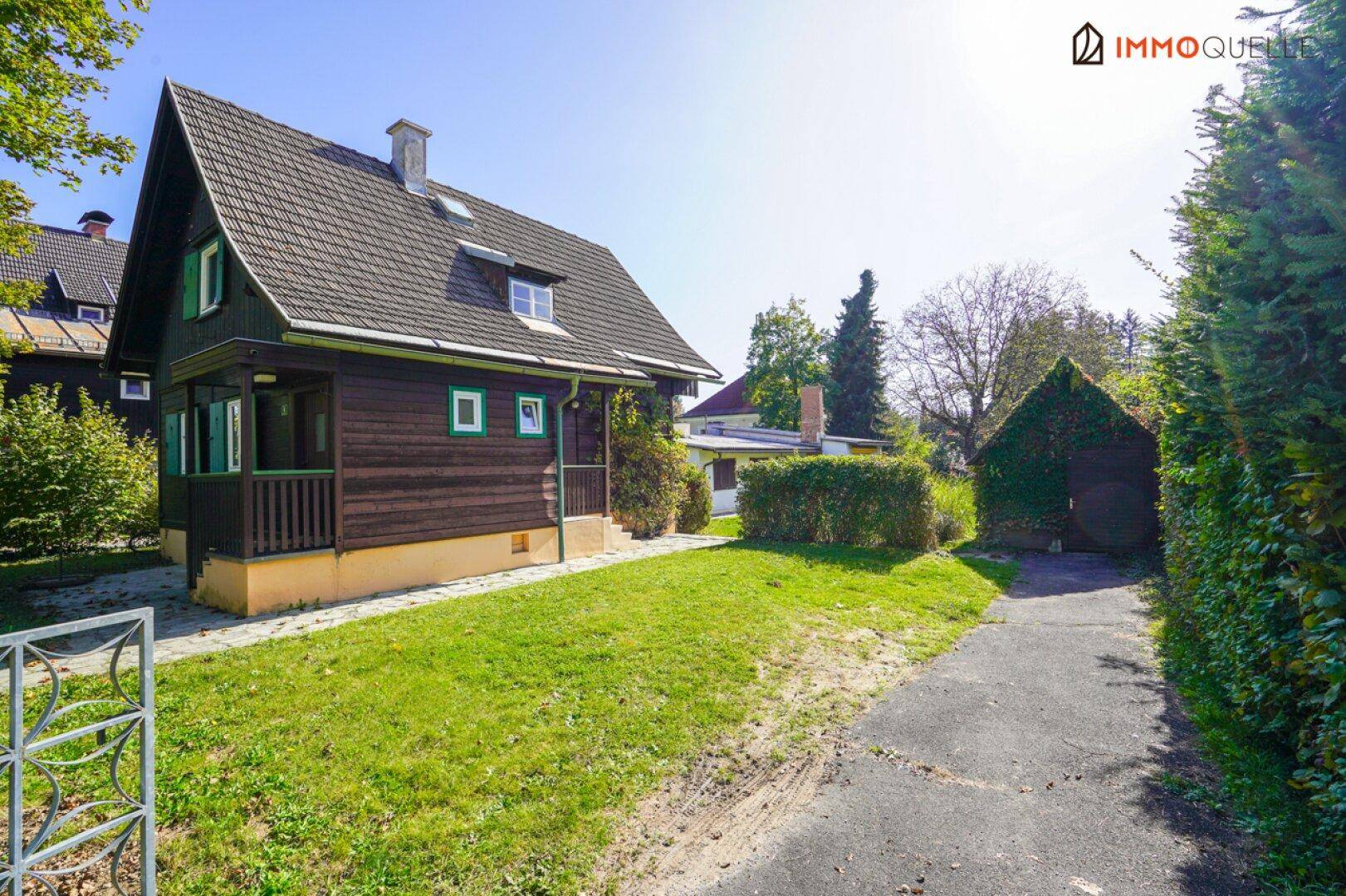 Charmantes Holzhaus mit Satteldach und grünem Gartenbereich an einem sonnigen Tag.
