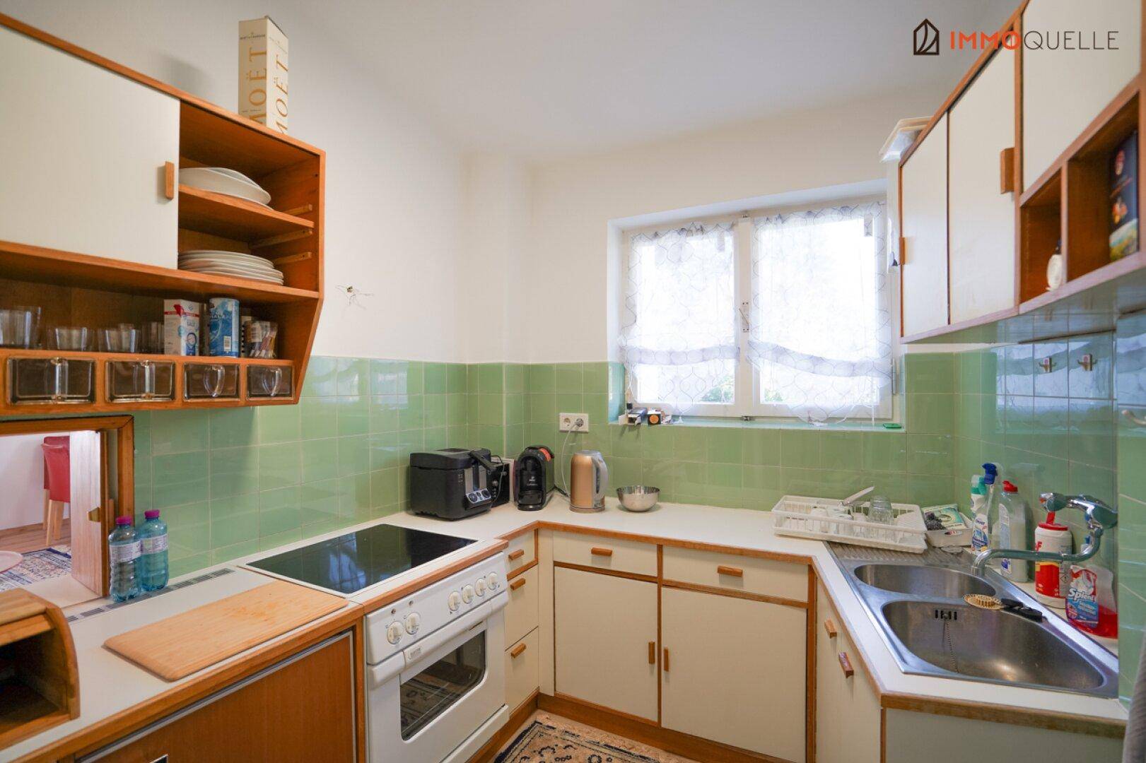 Funktionale Küche mit grünen Fliesen, Einbaugeräten und Fenster für natürliches Licht.