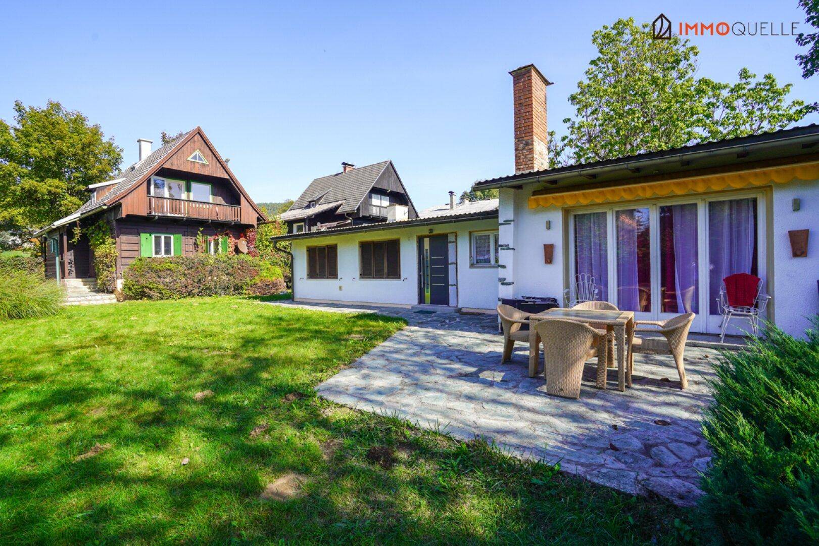Sonniger Terrassenbereich mit Gartenmöbeln und Blick auf den gepflegten Rasen und die umliegenden Häuser.