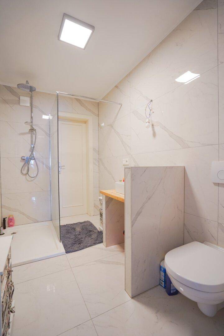Modernes Badezimmer mit großformatigen Fliesen, ebenerdiger Dusche und wandhängendem WC.