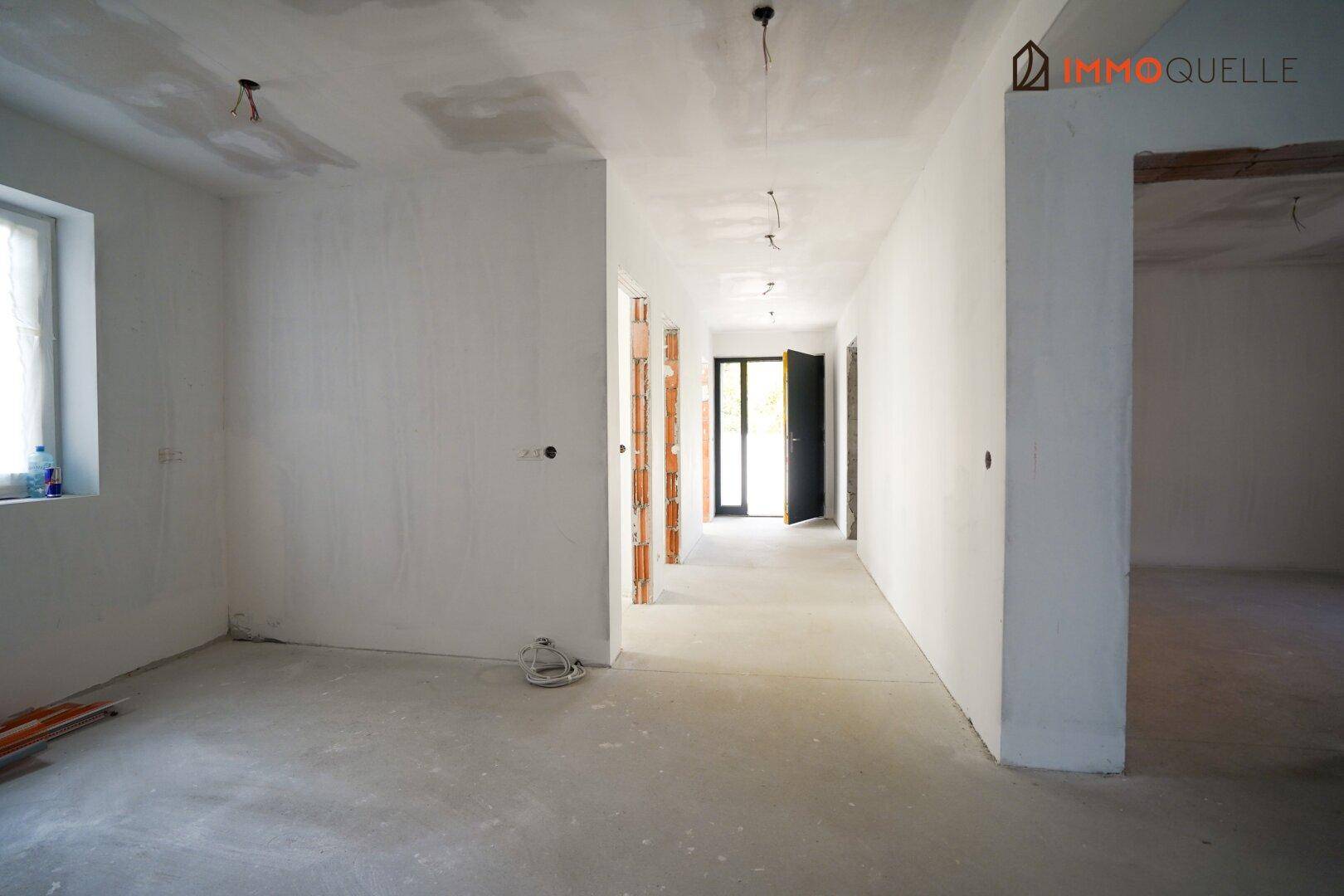 Langer Flur im Rohbauzustand mit Fenstern und Tür, bereit für den Innenausbau.