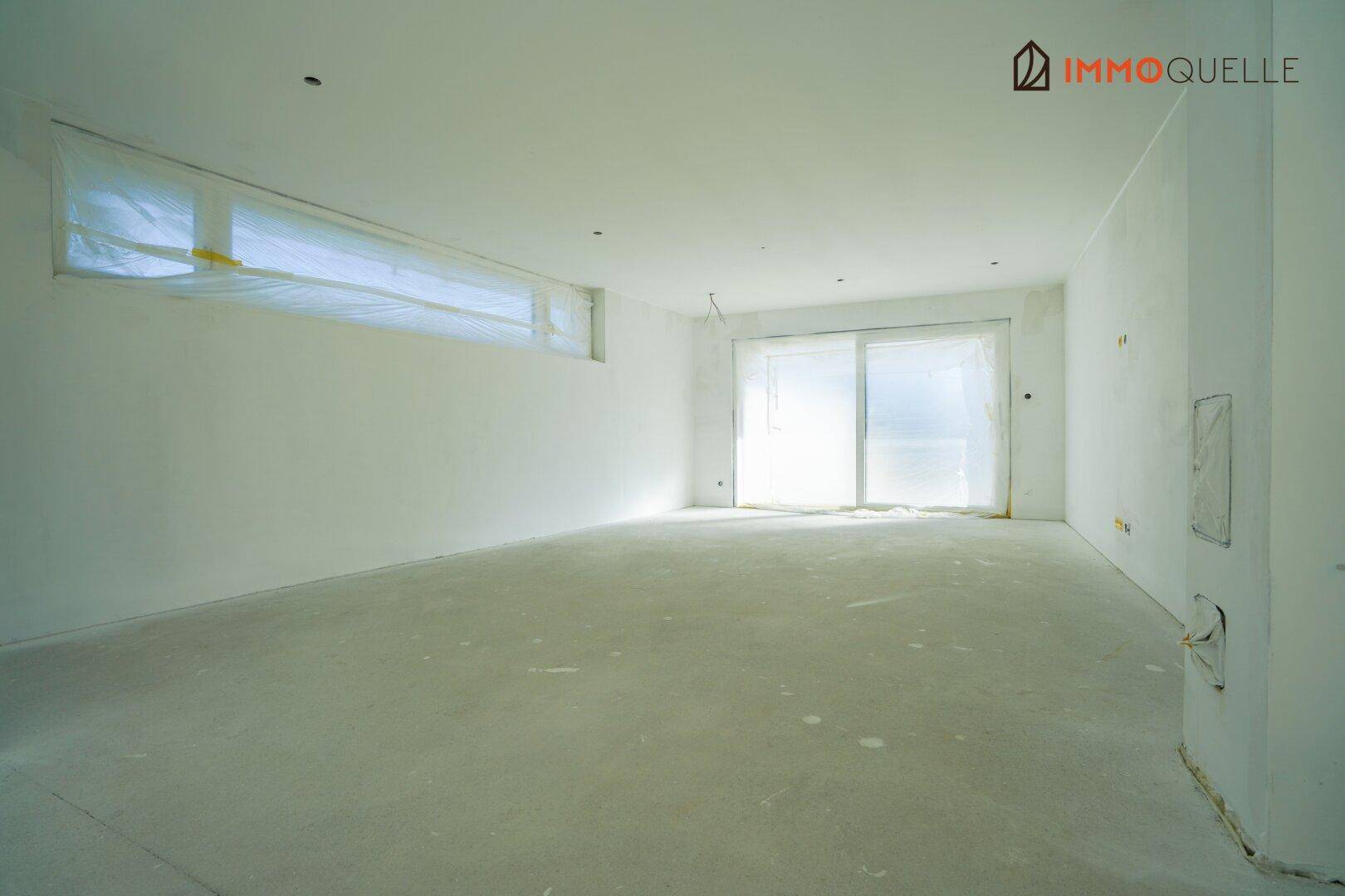 Großer, heller Raum im Rohbau mit Fenster und Terrassenzugang, wartet auf Fertigstellung.