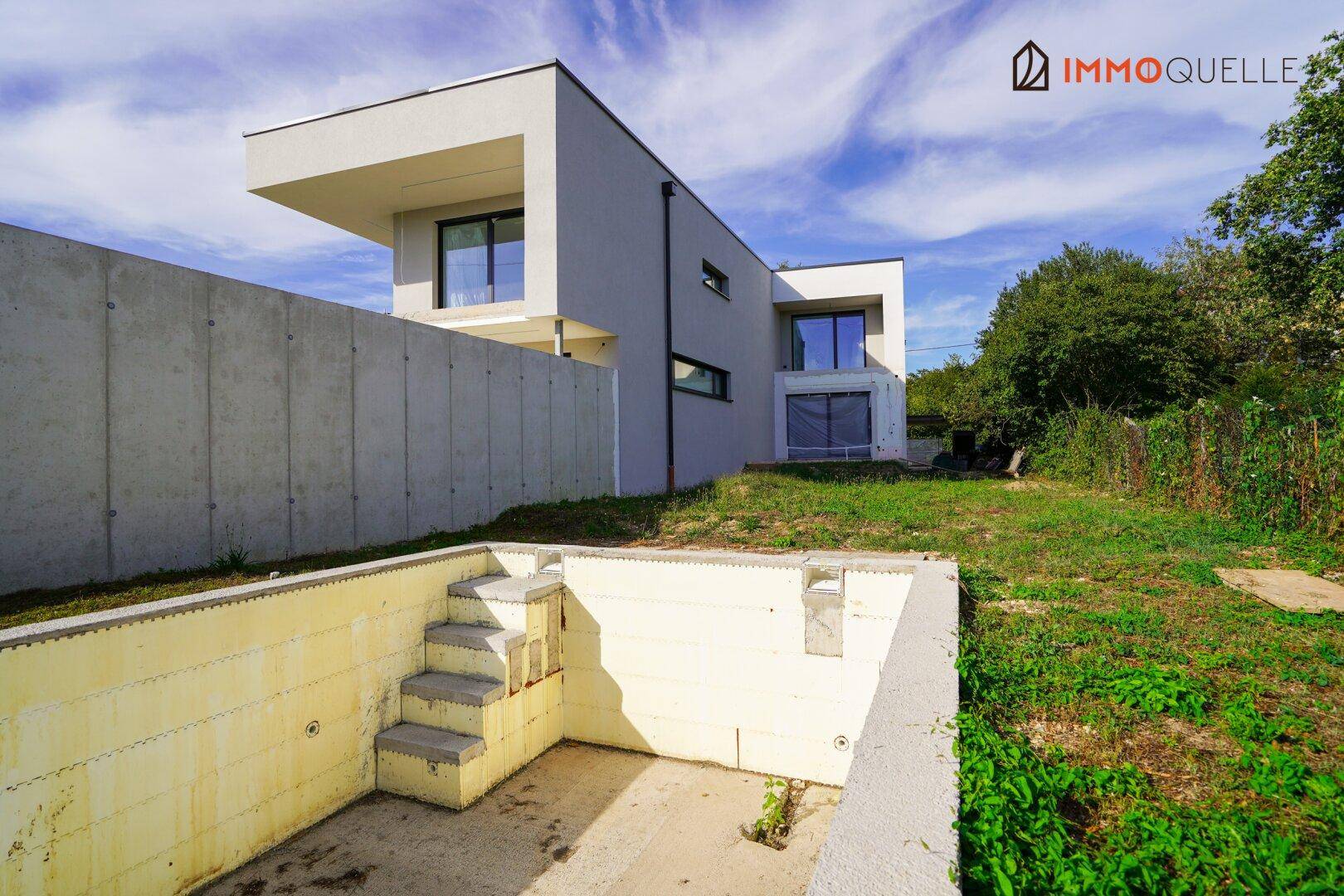 Moderne Hausfassade mit unfertigem Poolbereich und Betonmauer im Garten.