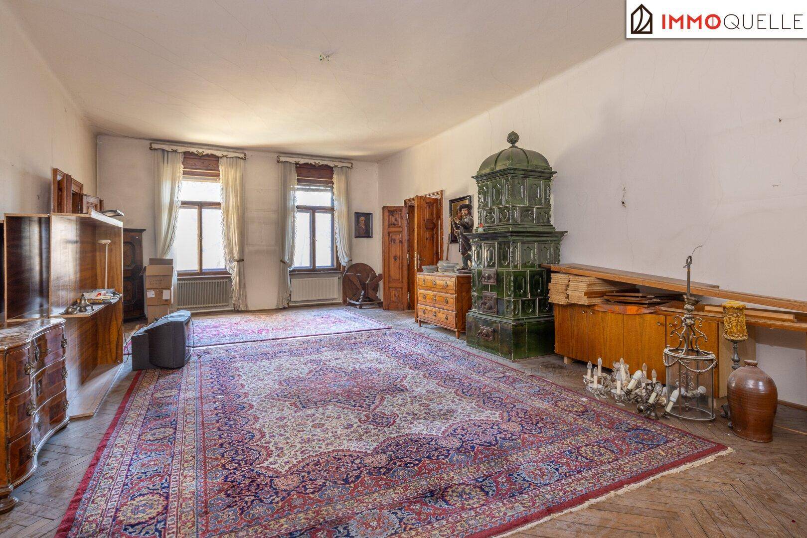 Geräumiges Wohnzimmer mit traditionellem Kachelofen und Fischgrätparkett in gutem Zustand.