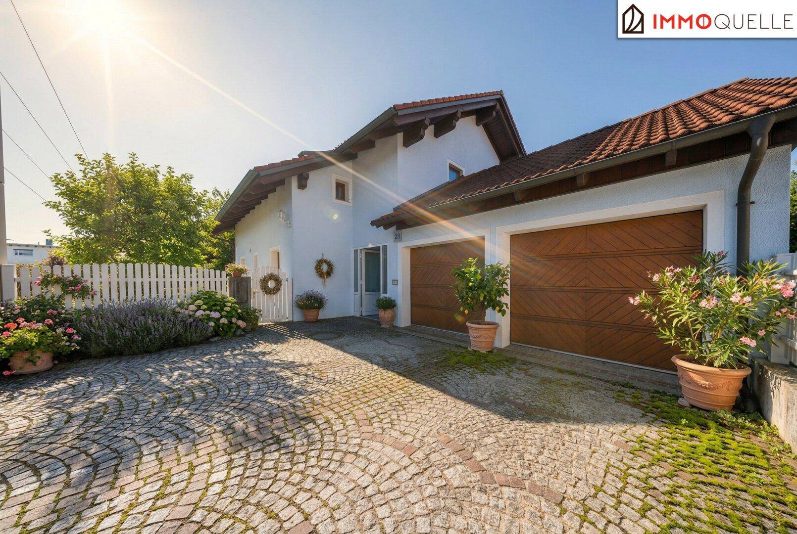 Vorderansicht des Hauses mit Doppelgarage, gepflasterter Auffahrt und Blumenbeeten.