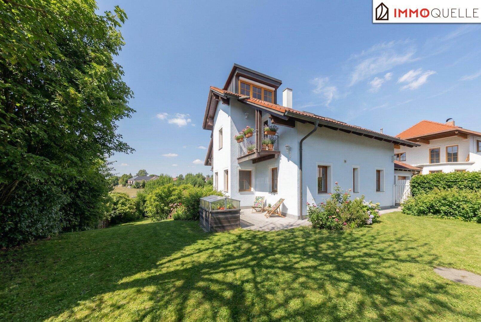Seitenansicht des Hauses mit weitläufigem Rasen, kleiner Terrasse und Blick ins Grüne.