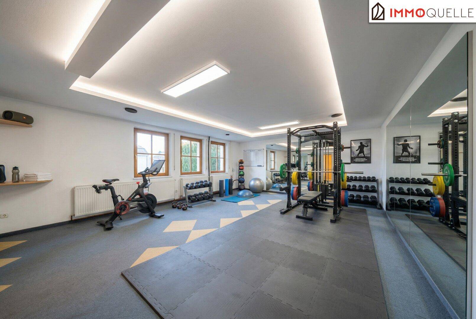 Gut ausgestatteter Fitnessraum mit verschiedenen Trainingsgeräten und Spiegelfront.