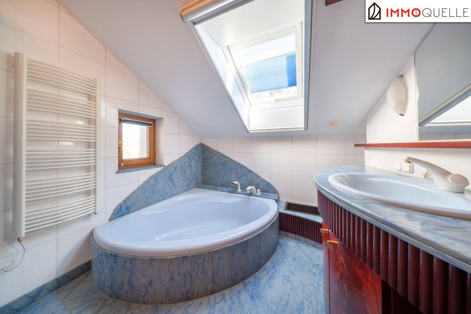 Badezimmer im Dachgeschoss mit Eckbadewanne, Dachfenster und blauen Fliesen.
