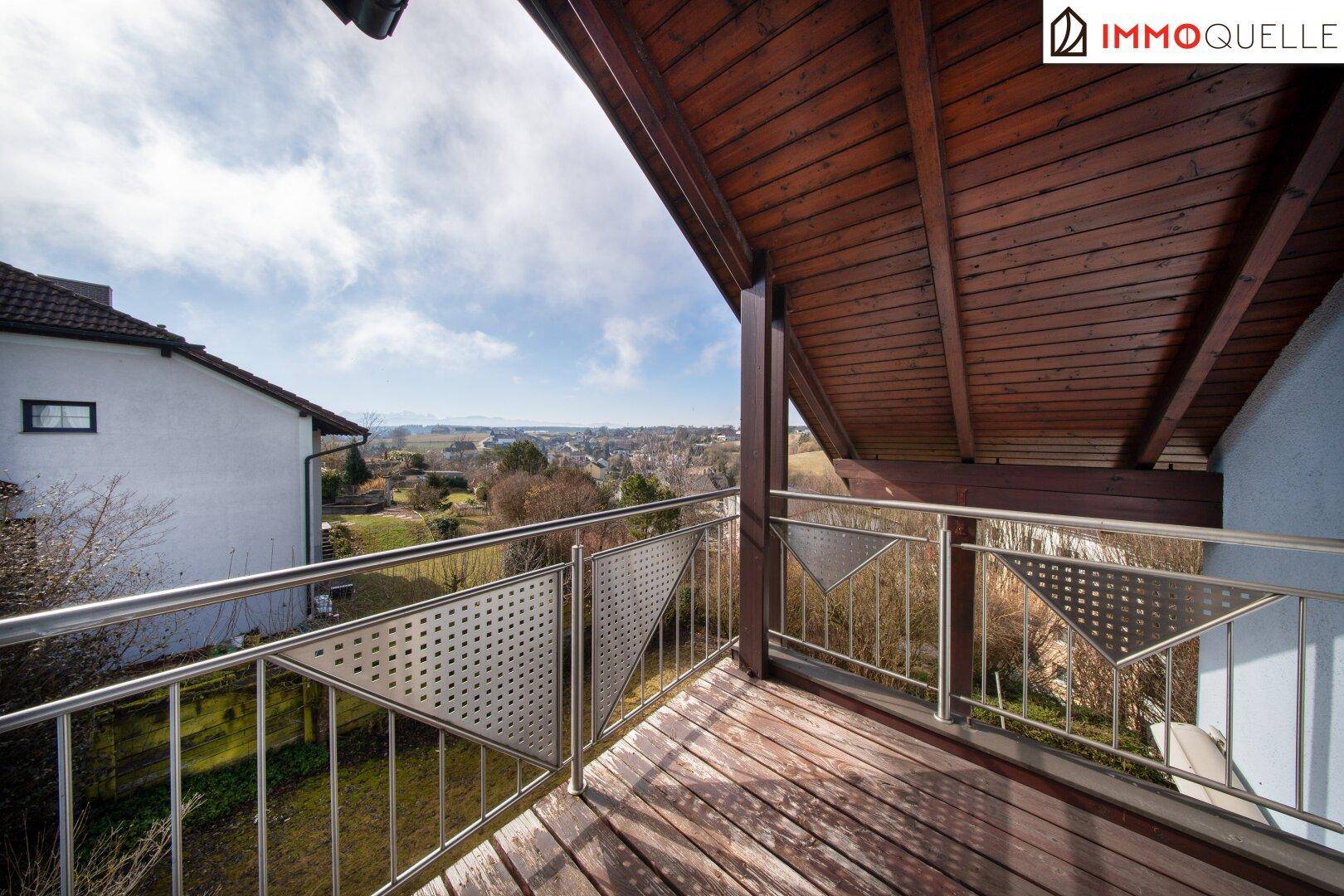 Überdachter Holzbalkon mit Metallgeländer und weitem Blick ins Grüne.