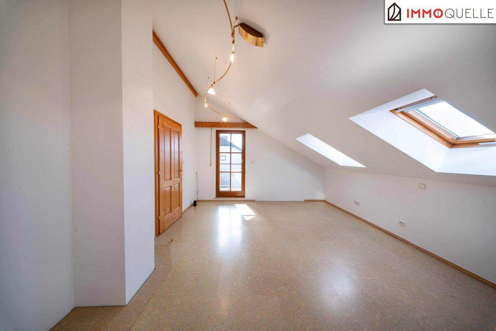 Geräumiges Zimmer im Dachgeschoss mit Holzboden, Dachfenstern und Zugang zum Balkon.