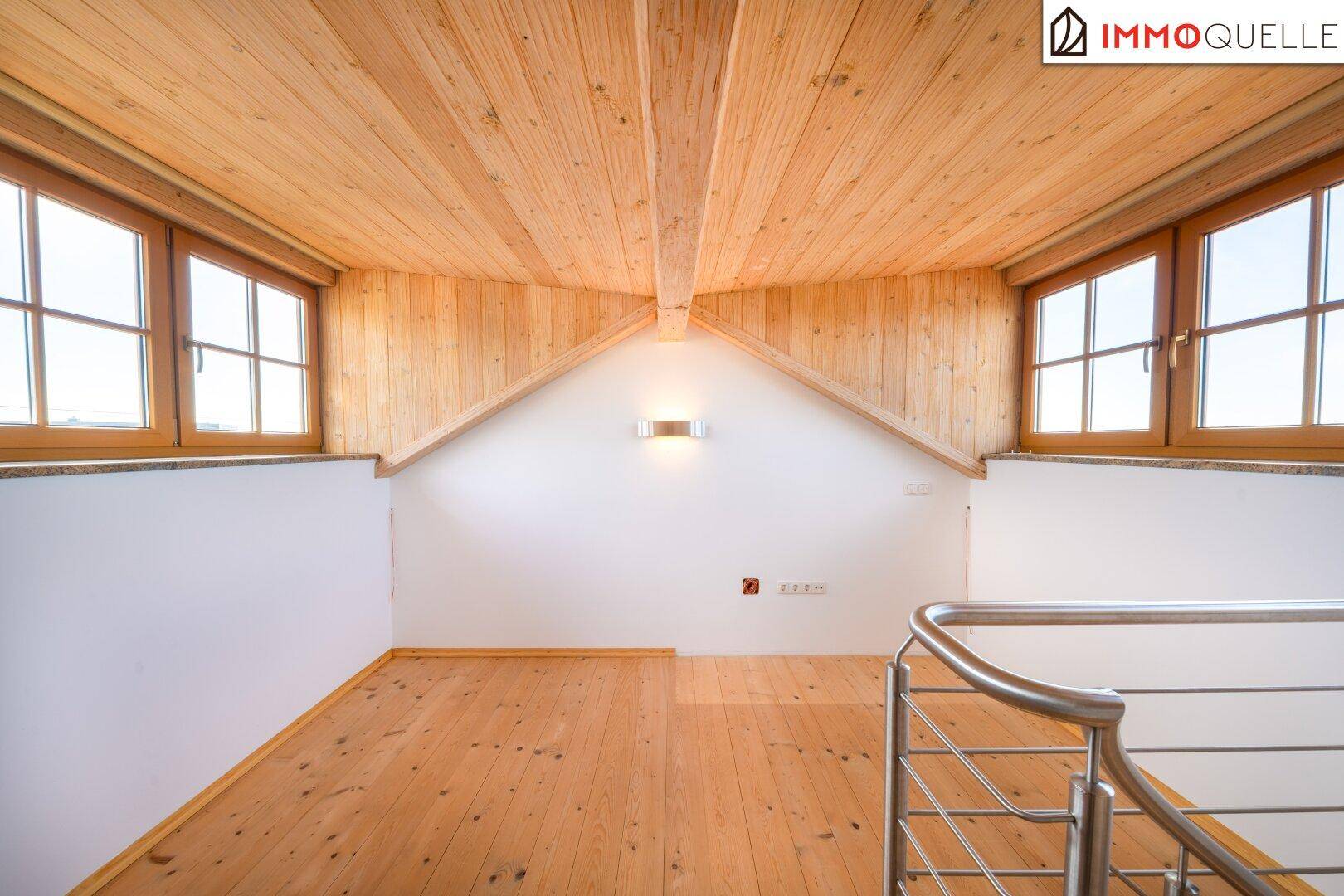 Offener Dachbodenbereich mit Holzbalken, großen Fenstern und Holzfußboden.