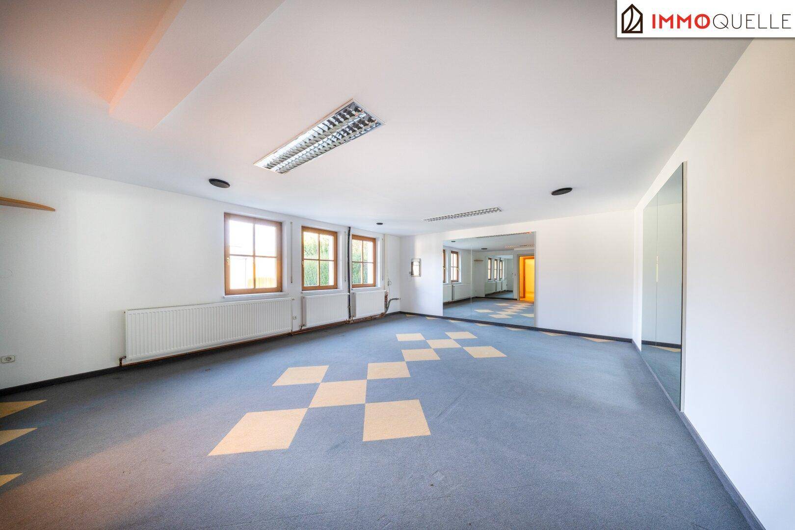 Geräumiger Fitnessraum mit Teppichboden und großer Spiegelfläche.