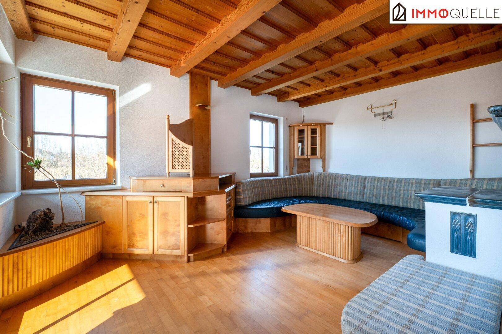 Gemütliches Wohnzimmer mit sichtbaren Holzbalken, Parkettboden und traditionellem Kachelofen.
