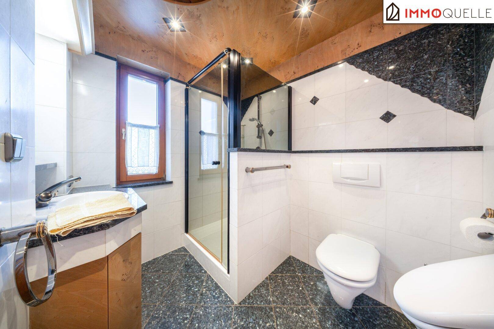 Modernes Badezimmer mit Dusche, WC und Fenster, ausgestattet mit dunklen Akzenten.