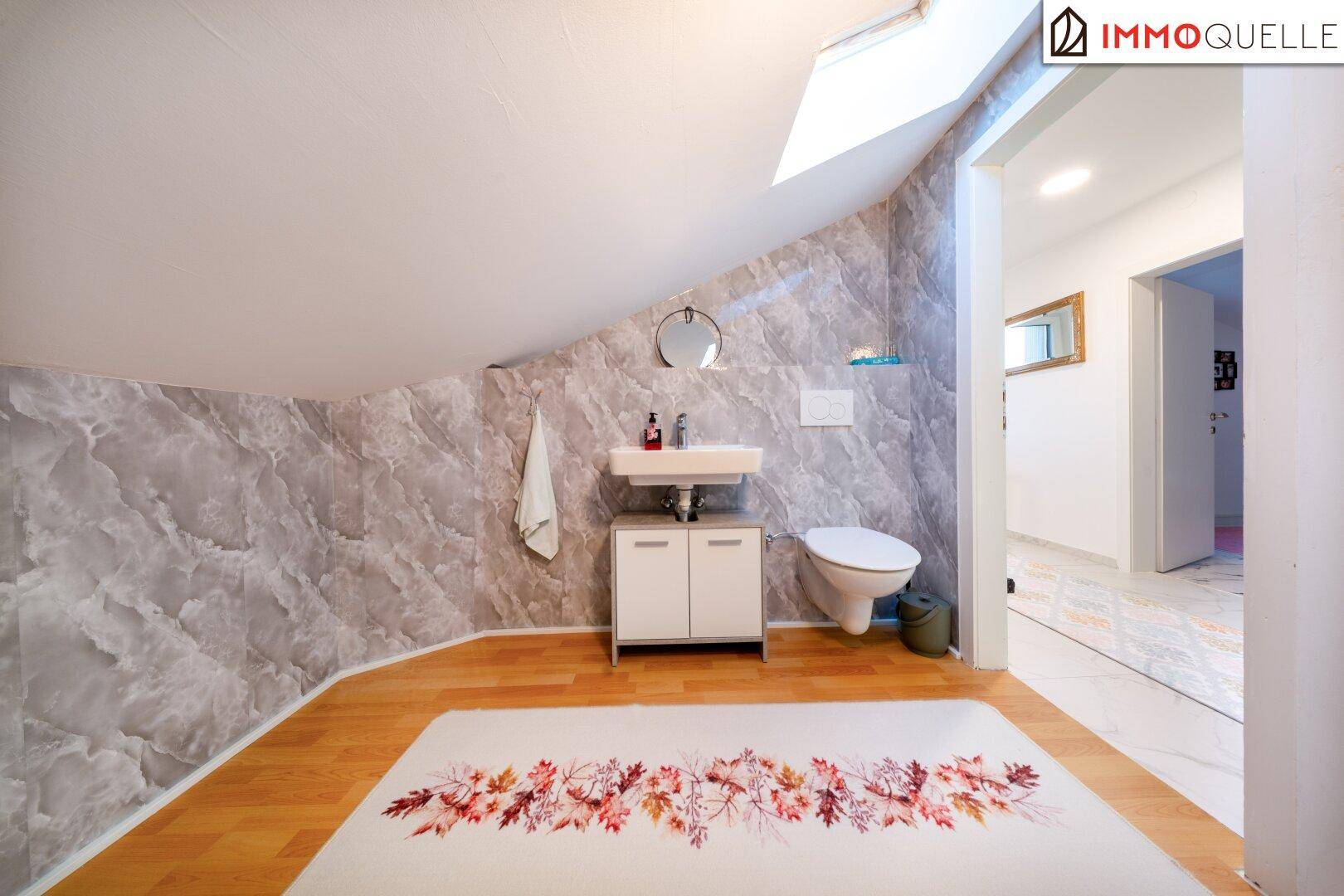 Modernes Badezimmer im Dachgeschoss mit Waschbecken, Toilette und Holzboden.