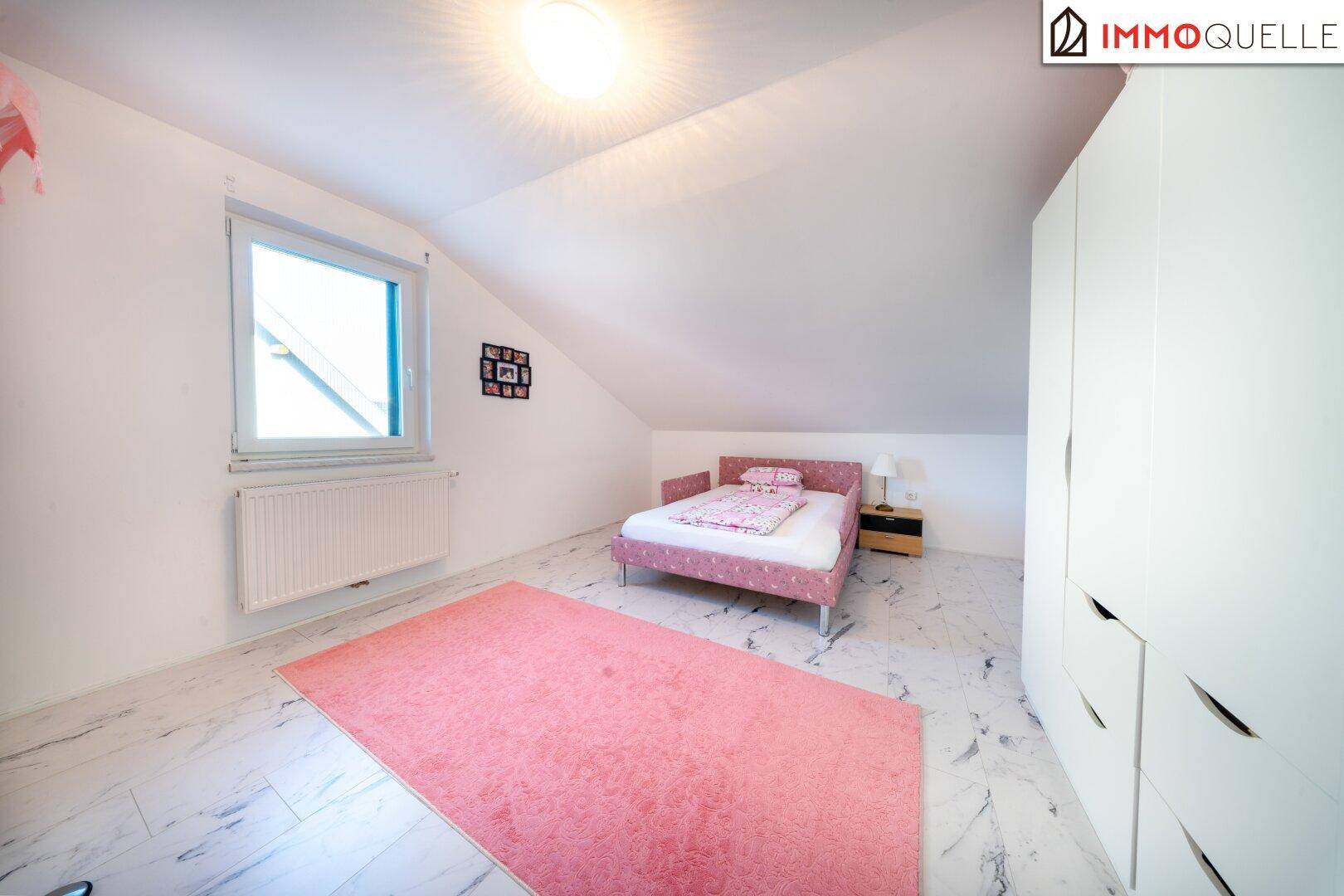 Helles Kinderzimmer mit rosa Teppich, Einzelbett und Dachschräge mit Fenster.