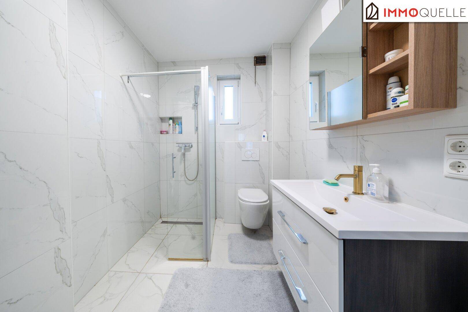 Modernes Badezimmer mit begehbarer Dusche, wandhängender Toilette und Marmorfliesen.