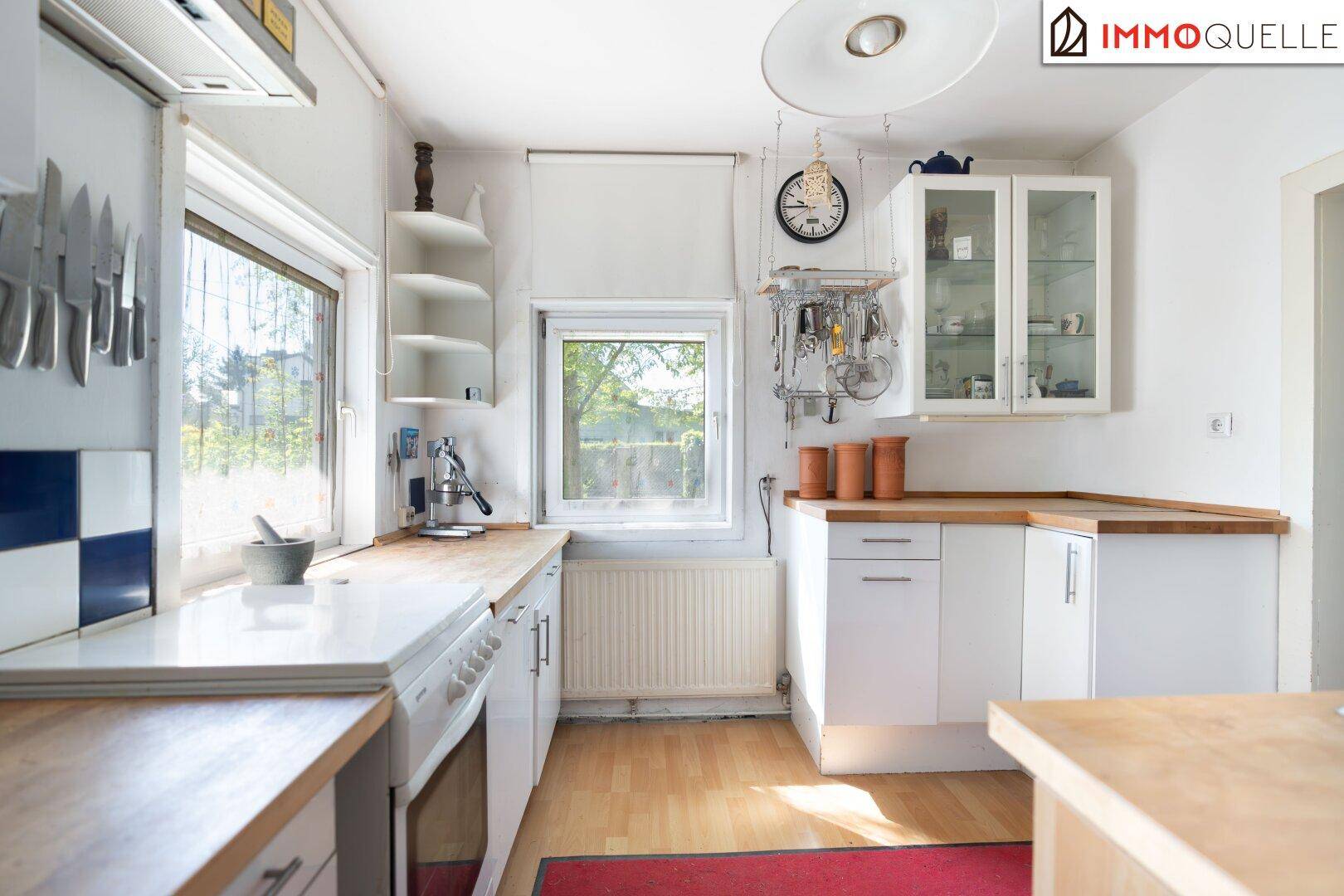 Gemütliche Küche mit Holz-Arbeitsplatten, weißen Schränken und viel Tageslicht durch die Fenster.