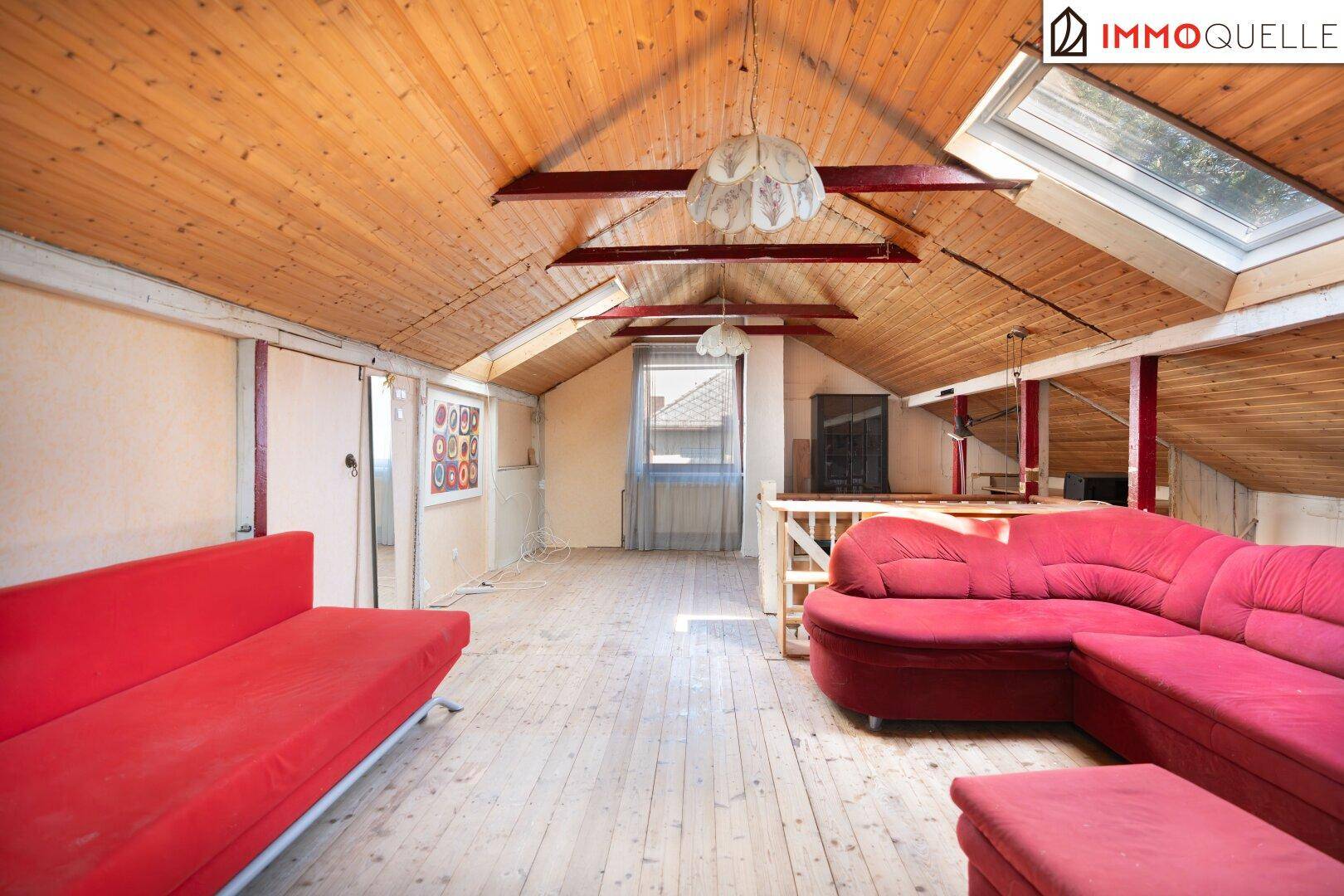 Geräumiger Dachboden mit Holzboden, roten Sofas und viel Tageslicht durch die Fenster.