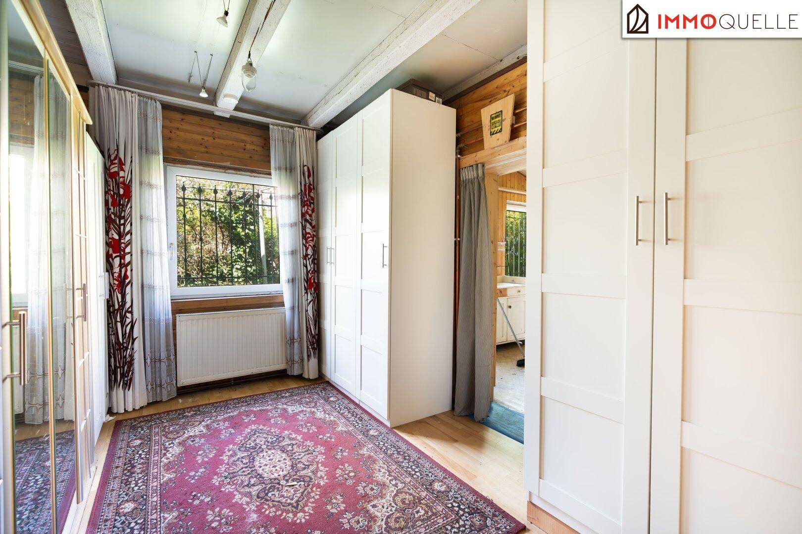 Schlafzimmer mit Holzvertäfelung, Parkettboden und weißen Einbauschränken.