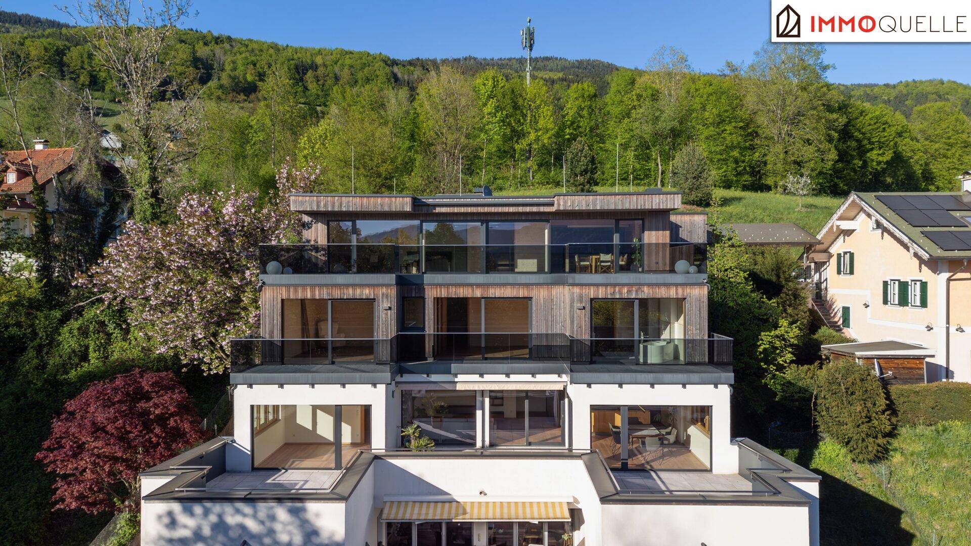 Moderne Wohnanlage mit mehreren Terrassen und großen Glasfronten in grüner Umgebung.