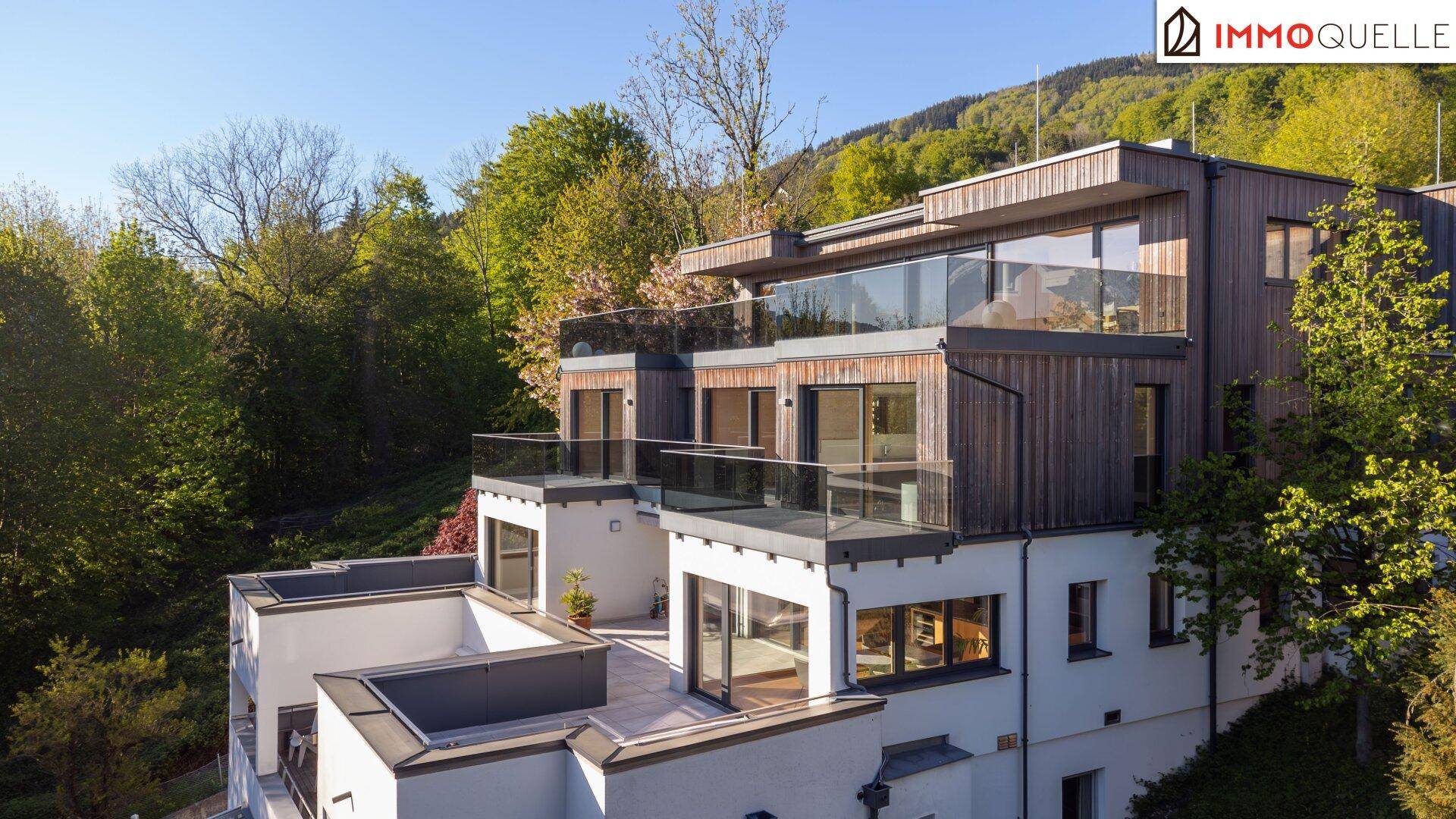 Architektonisch ansprechendes Gebäude mit Holzfassade, Glasbalkonen und Bergblick.