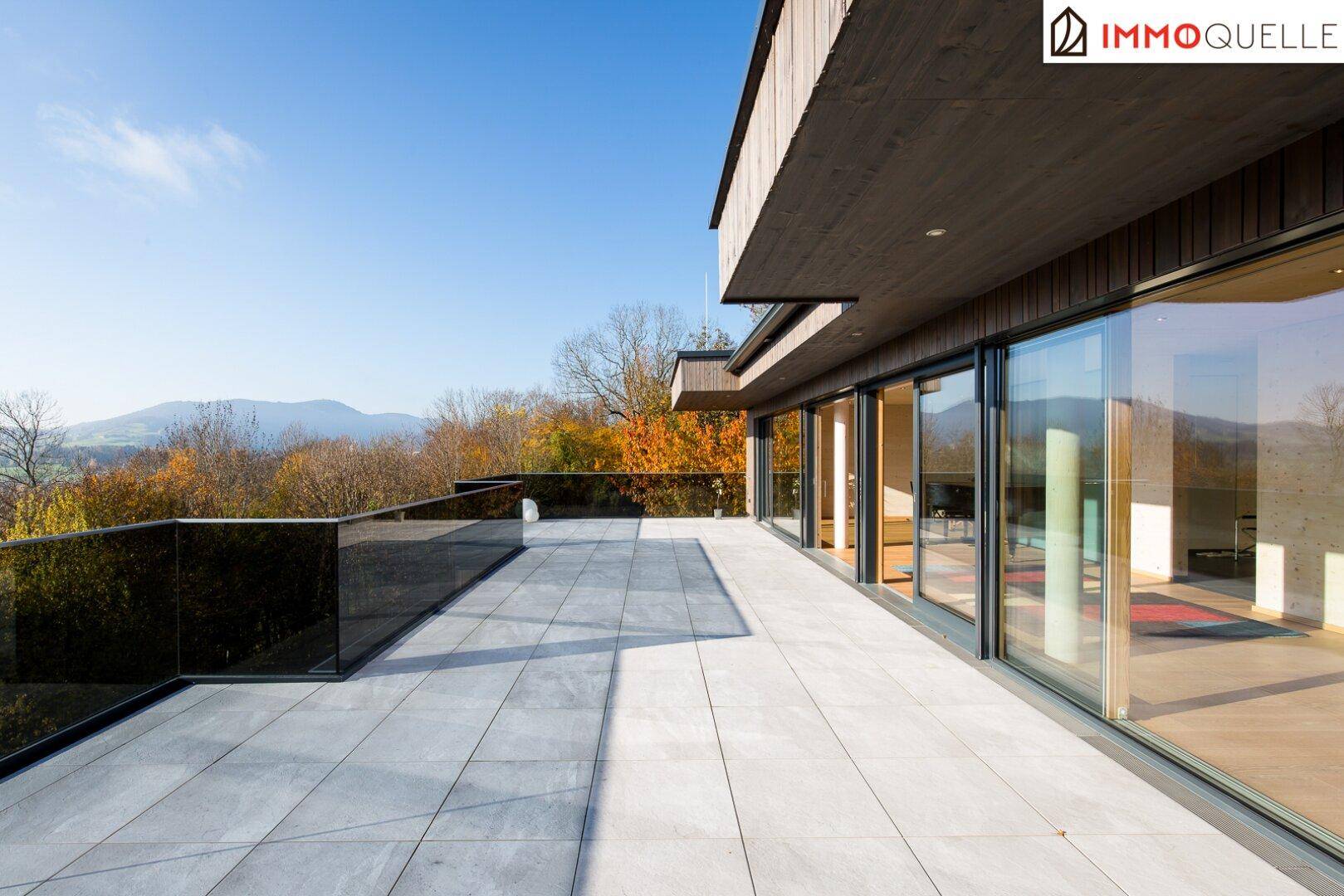 Sonniger Terrassenbereich mit Fliesenboden und Glasgeländer, umgeben von herbstlicher Natur und Bergblick.