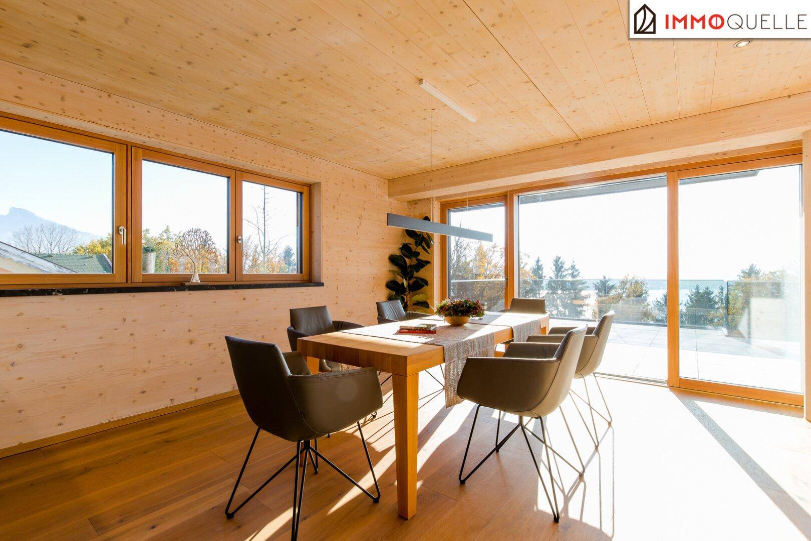 Sonniger Essbereich mit Holzwänden, Parkettboden und großen Fenstern mit Blick auf die Landschaft.