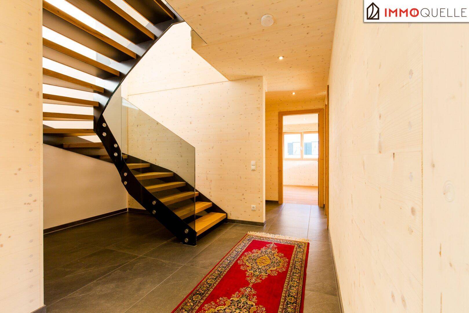 Eleganter Flur mit moderner Treppe, Fliesenboden und Holzwänden, die zu den oberen Etagen führt.